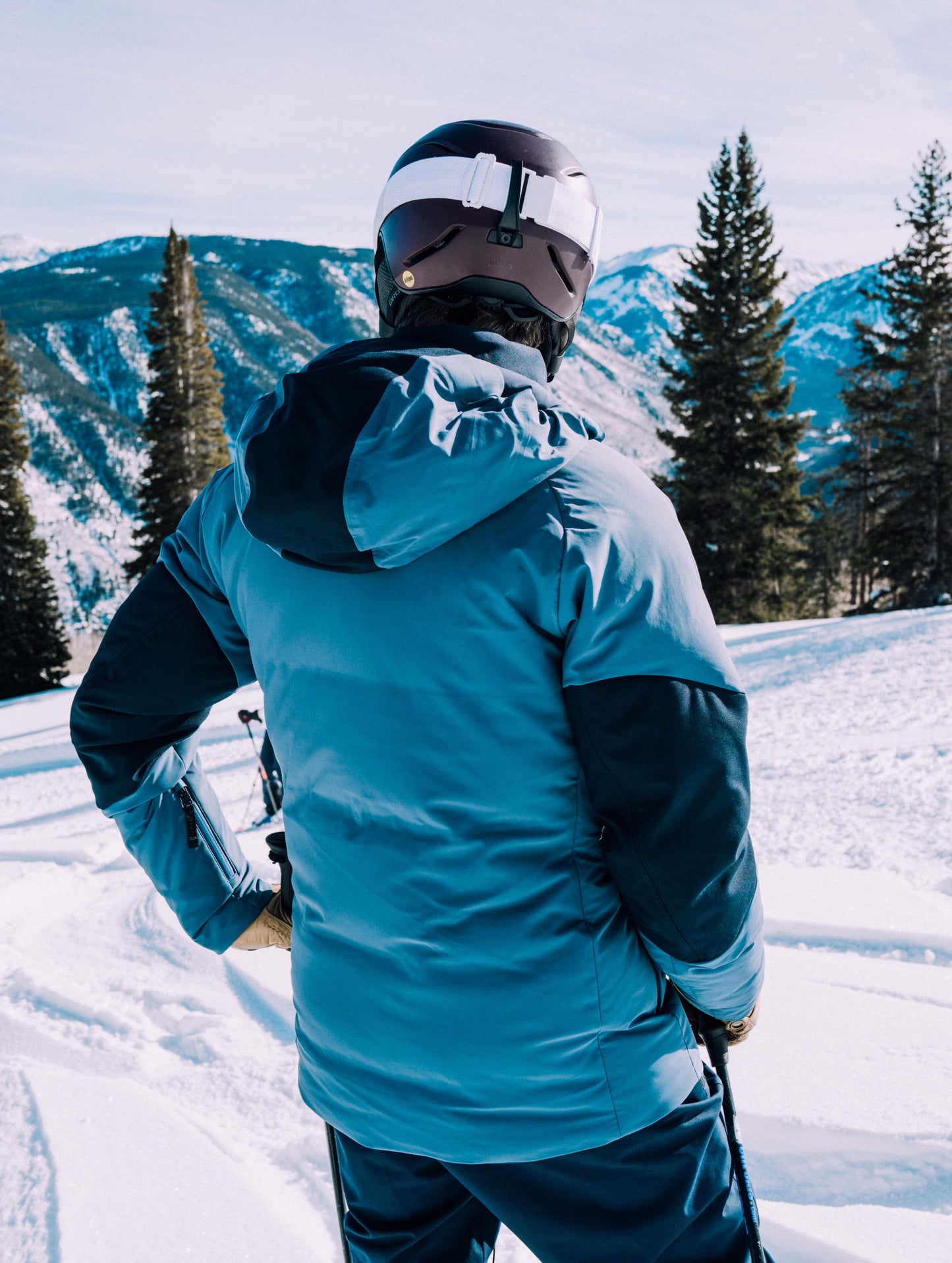 Outdoor lifestyle image of back of man on snowcovered hill wearing Torino Jacket in Baltic Blue from AETHER Apparel.
