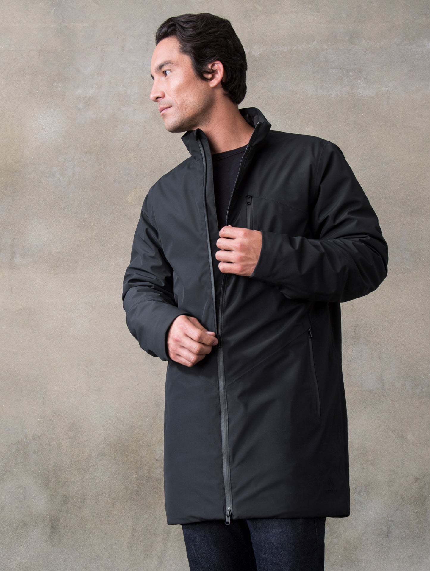 Man indoors wearing and unzipping black Tundra Jacket from ATHER Apparel.