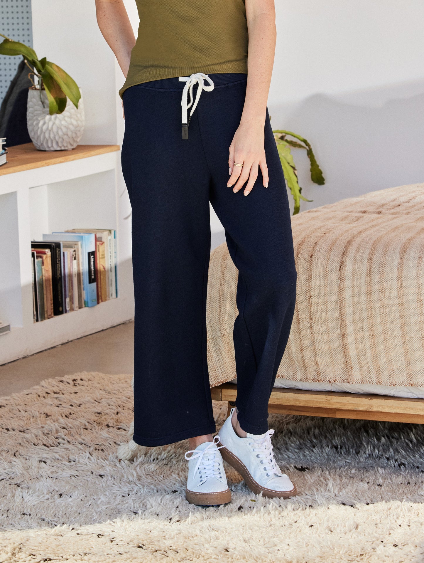 Indoor lifestyle image of woman standing in bedroom wearing Dalton Low-Top Sneaker in White from AETHER Apparel.