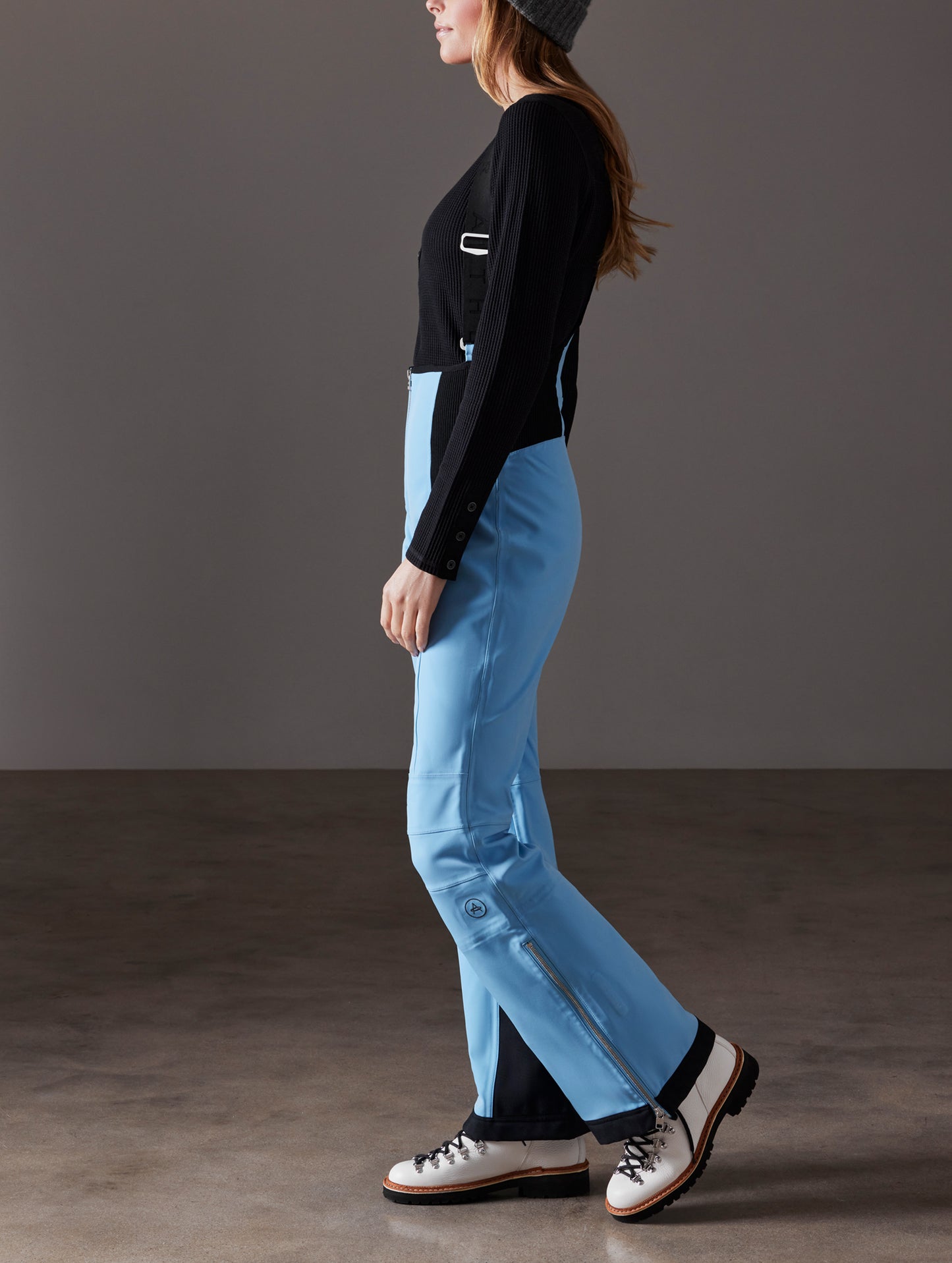 Side profile full-body view of woman wearing Descent Snow Bib 2.0 in Atlas Blue from AETHER Apparel.