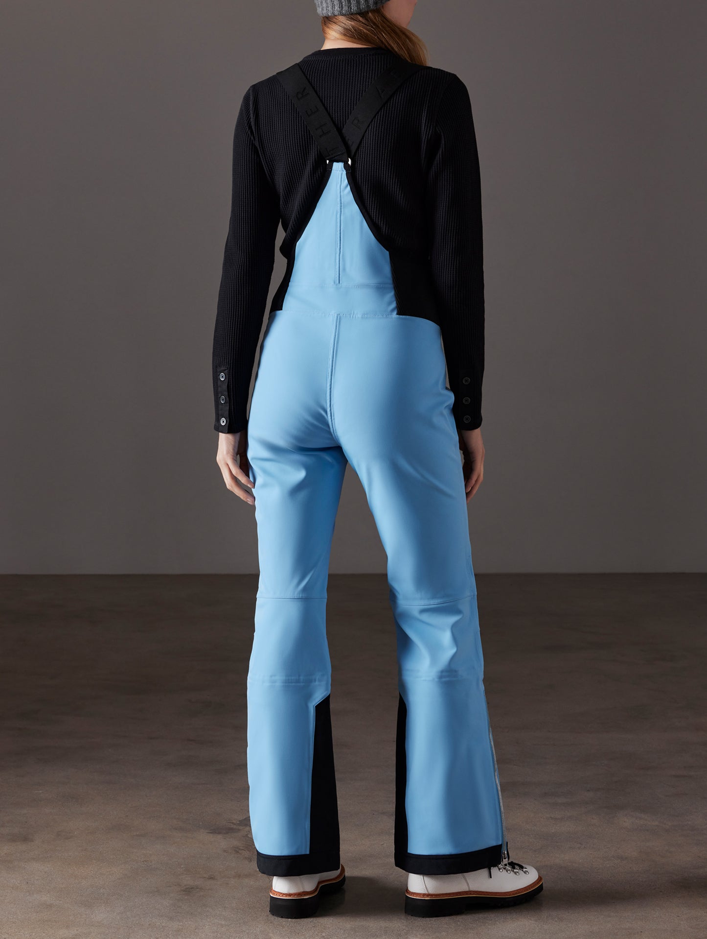 Rear full-body view of woman wearing Descent Snow Bib 2.0 in Atlas Blue from AETHER Apparel.