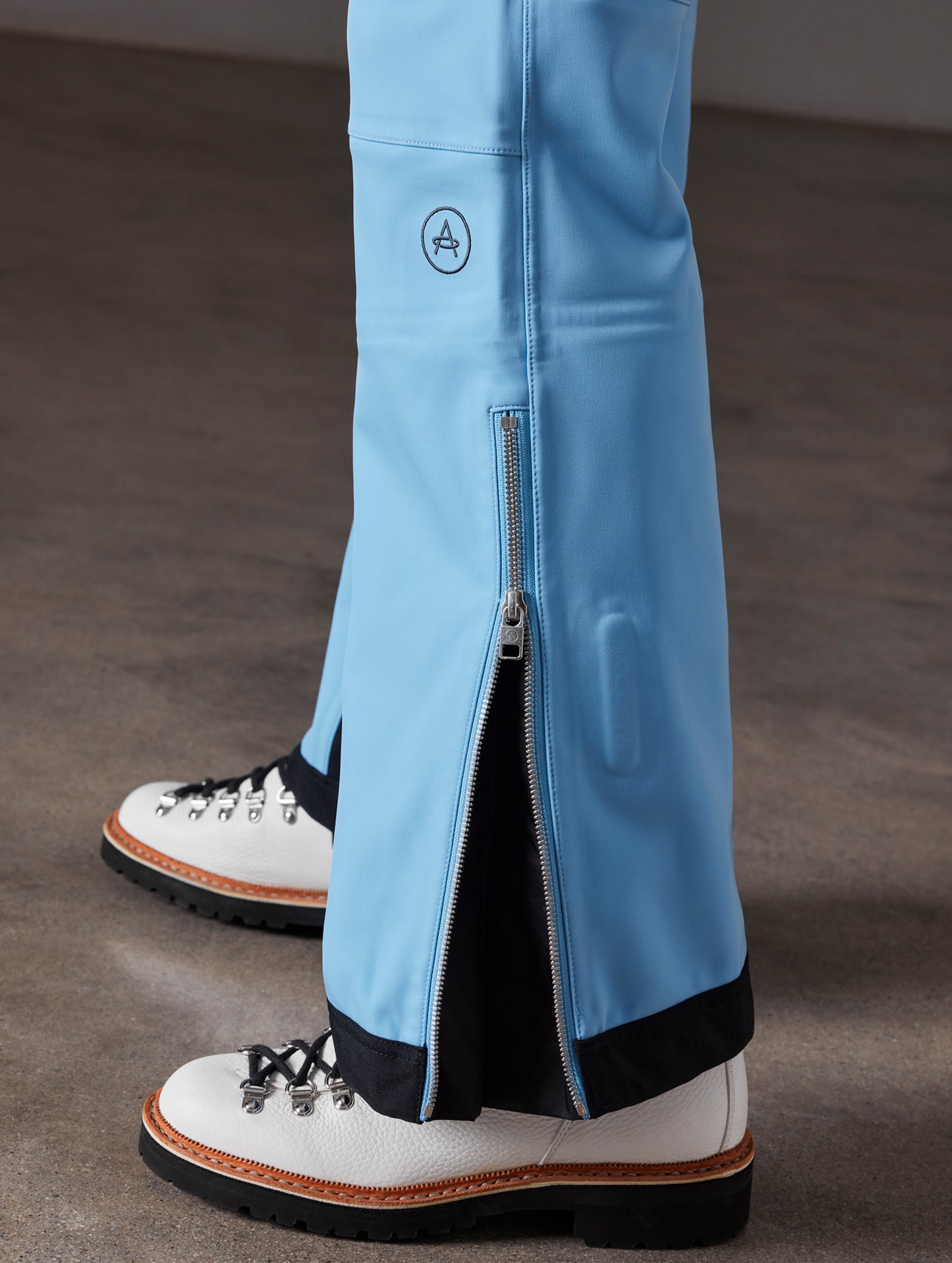 Closeup detailed view of zippered leg cuffs and AETHER logo on women's Descent Snow Bib 2.0 in Atlas Blue from AETHER Apparel.