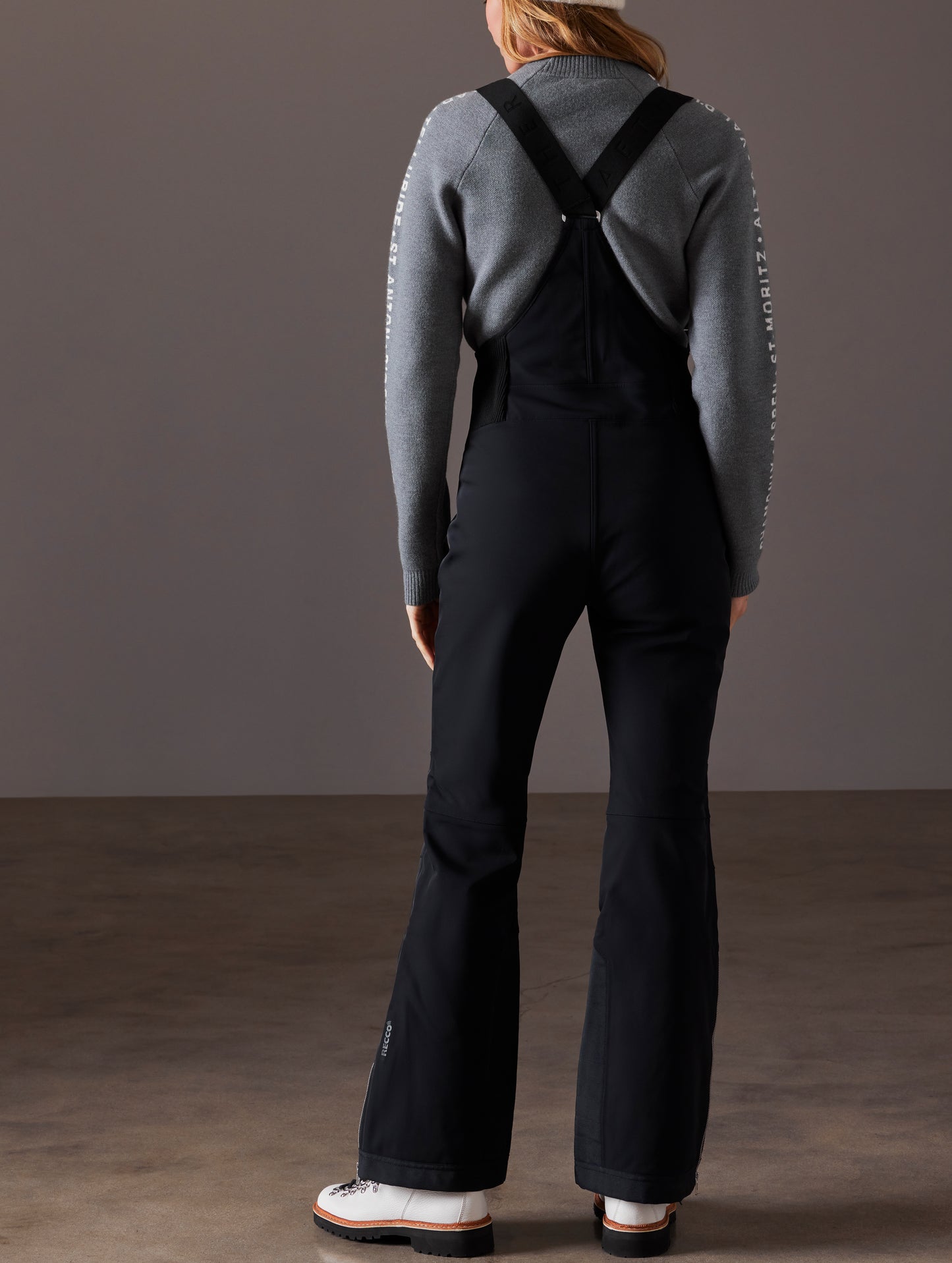 Rear full-body view of woman wearing Descent Snow Bib 2.0 in Onyx Black from AETHER Apparel.