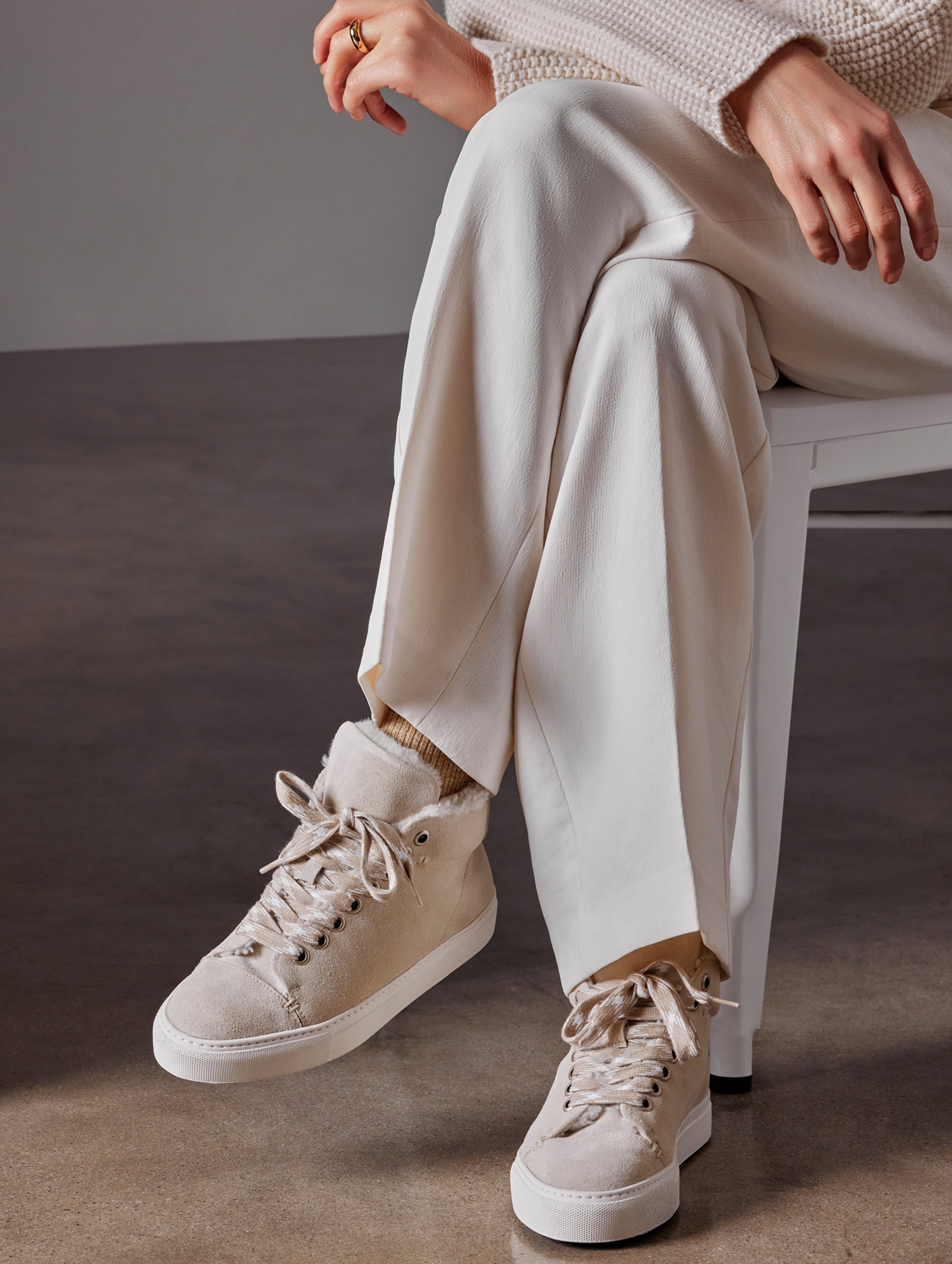 Front angled view of woman sitting in chair with legs crossed wearing Durham Sneaker with Shearling in Bone white from AETHER Apparel.