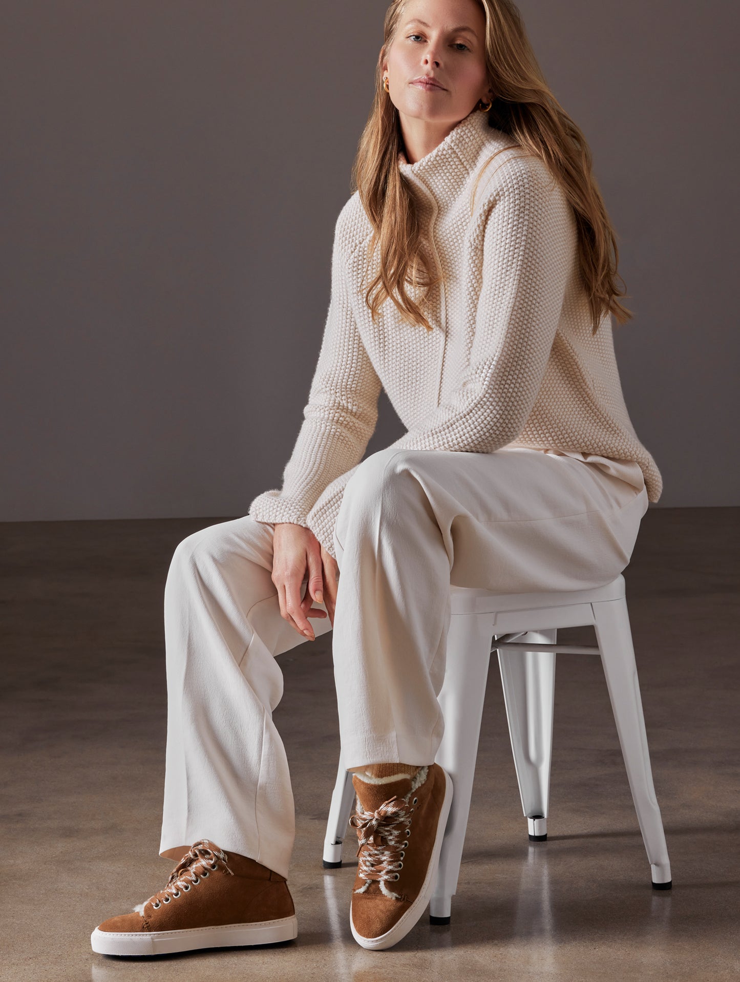 Front angled full-body view of woman sitting in chair wearing Durham Sneaker with Shearling in Canyon Tan from AETHER Apparel.