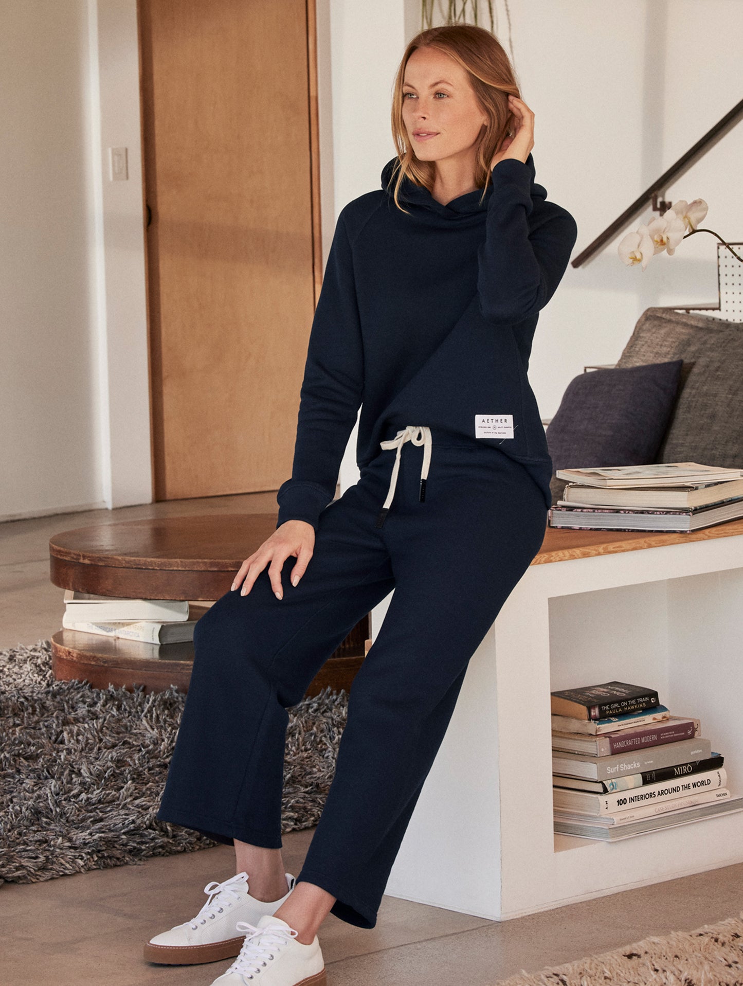 Front angled full-body view of woman wearing Foundation Hoodie in Nordic Navy blue from AETHER Apparel.