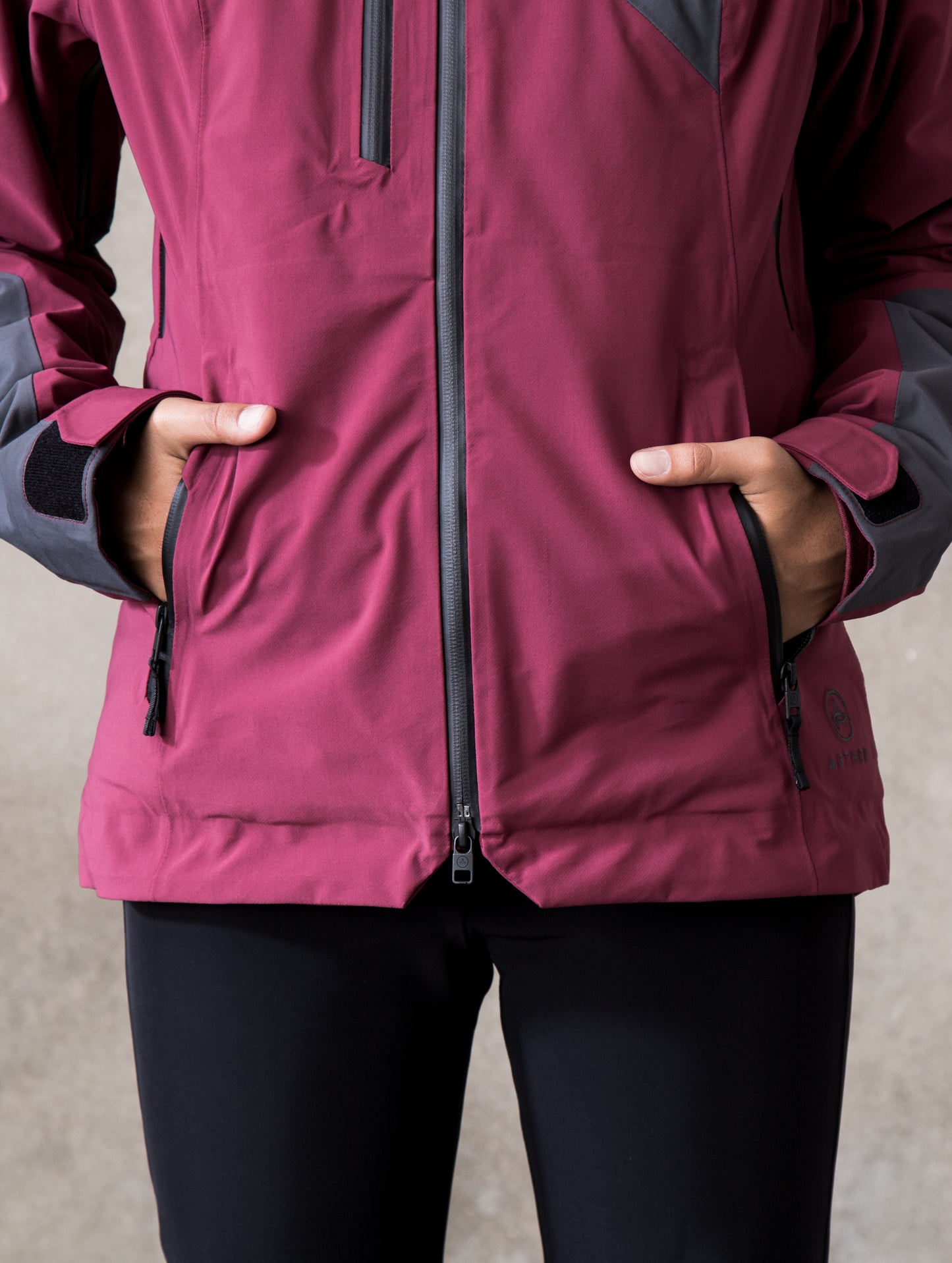 Woman wearing dark red Fusion Jacket from AETHER Apparel, displaying open hand pockets.