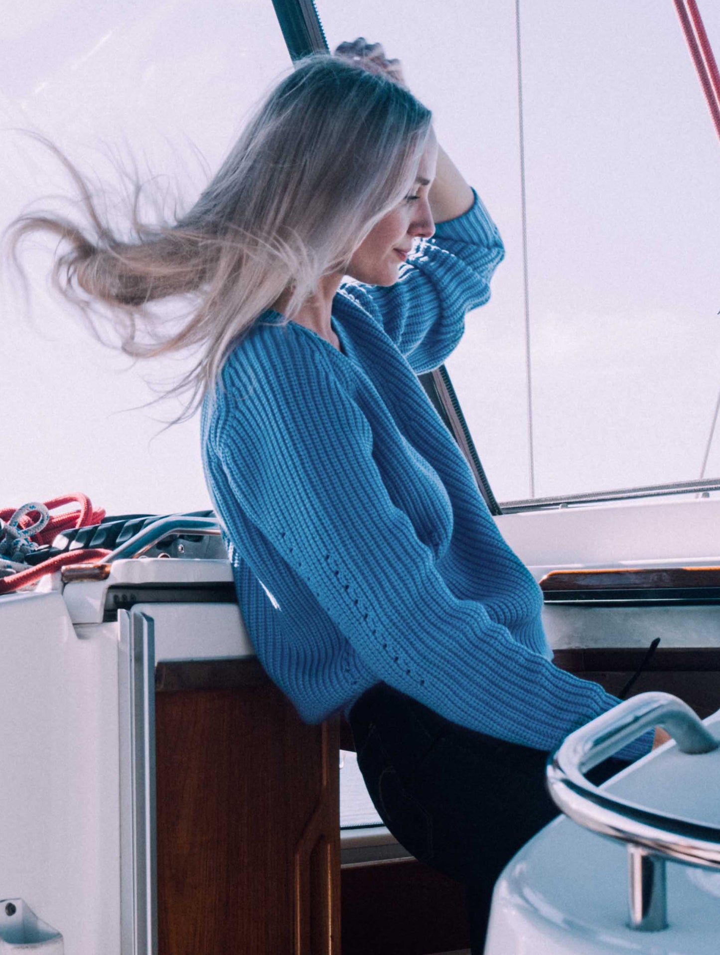 Side view of woman on boat wearing light blue Keaton Sweater from AETHER Apparel.