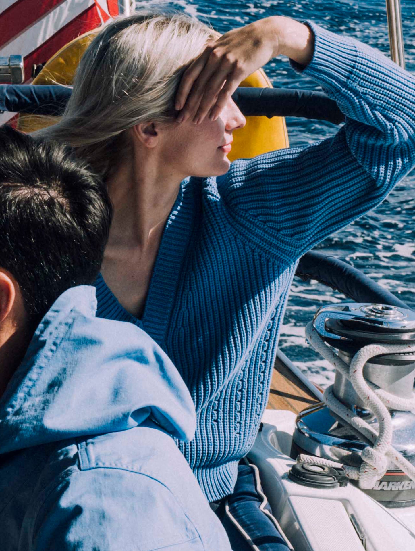 Woman sitting on boat wearing light blue Keaton Sweater from AETHER Apparel.