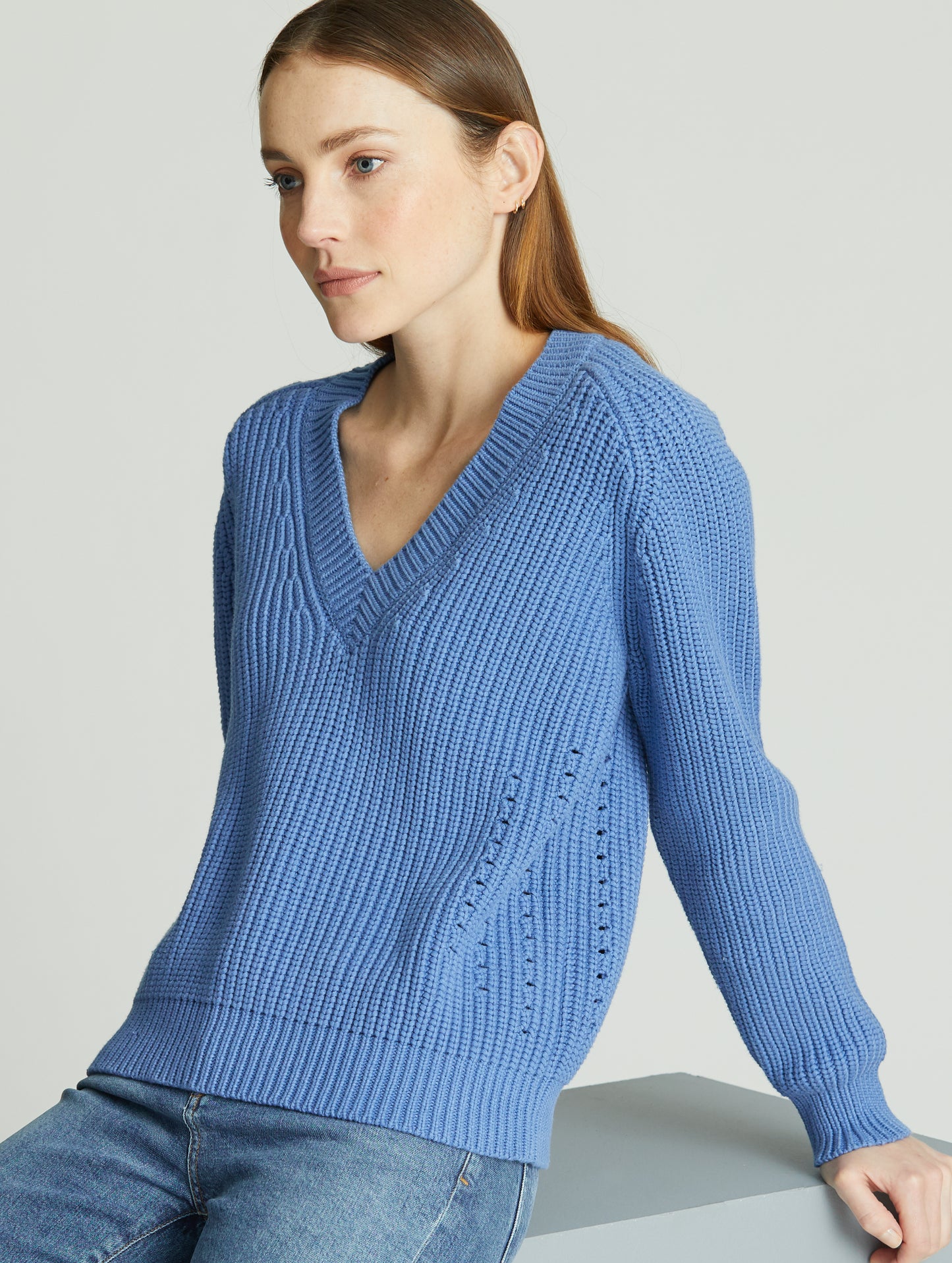 Woman indoors sitting wearing light blue Keaton Sweater from AETHER Apparel.