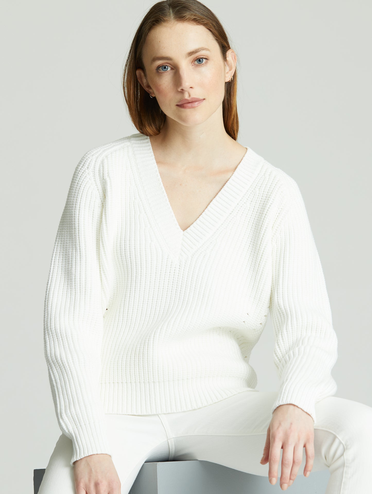 Woman sitting wearing white Keaton Sweater from AETHER Apparel.