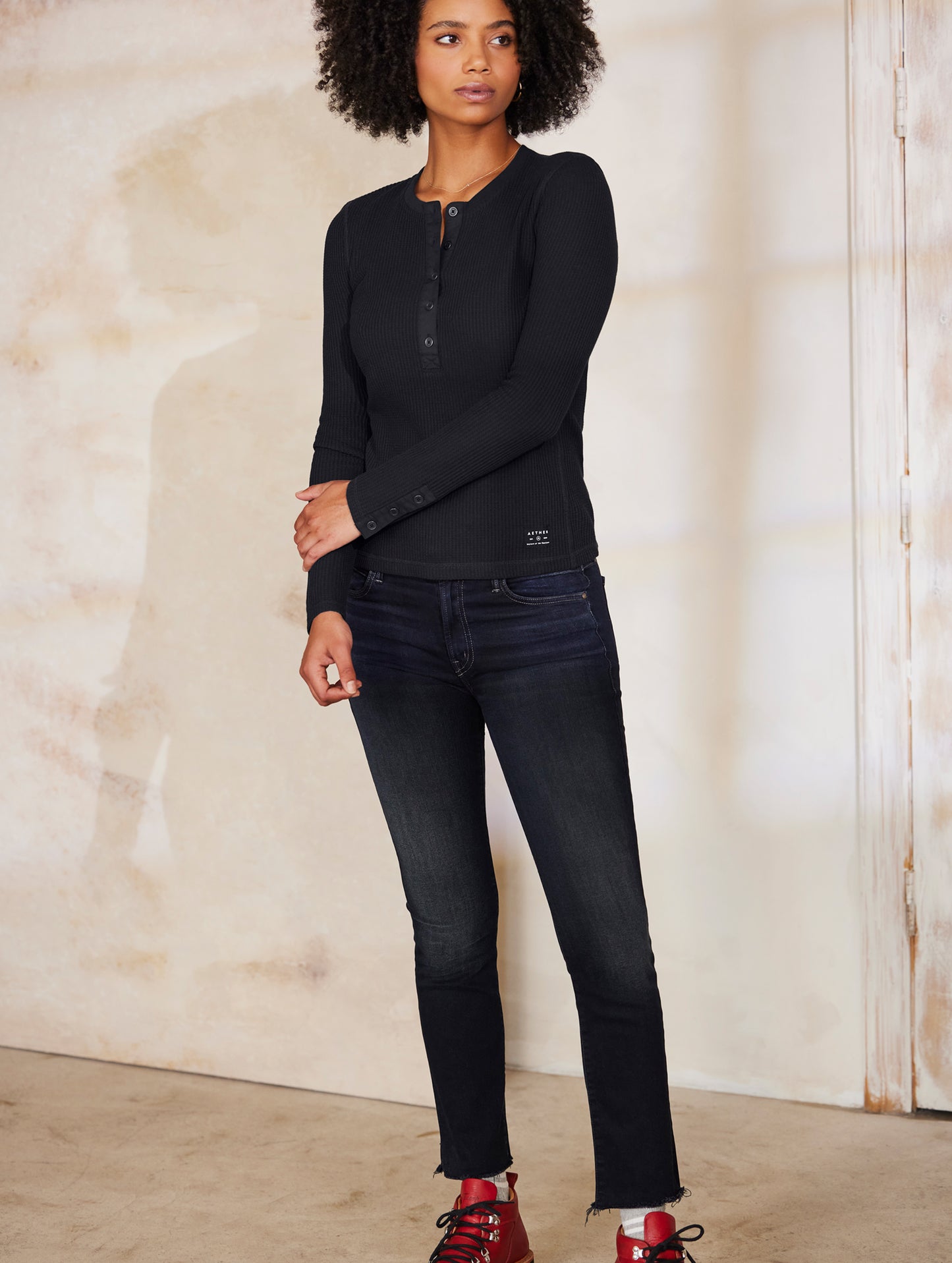 Full body view of woman wearing black Long Sleeve Waffle Henley from AETHER Apparel.
