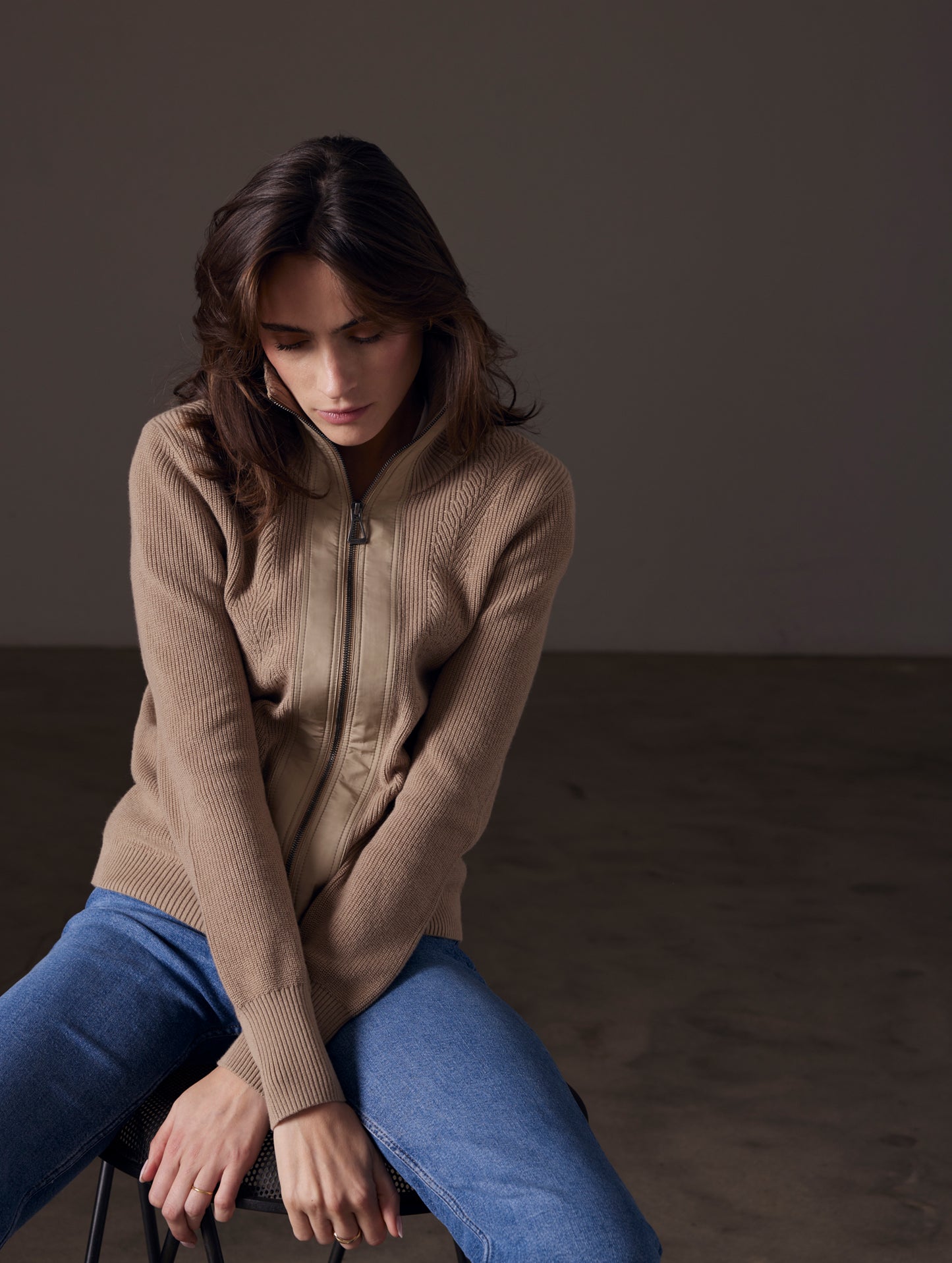 Front view of woman sitting on stool with crossed arms wearing Rhea Full-Zip Sweater in Chinchilla Brown from AETHER Apparel.