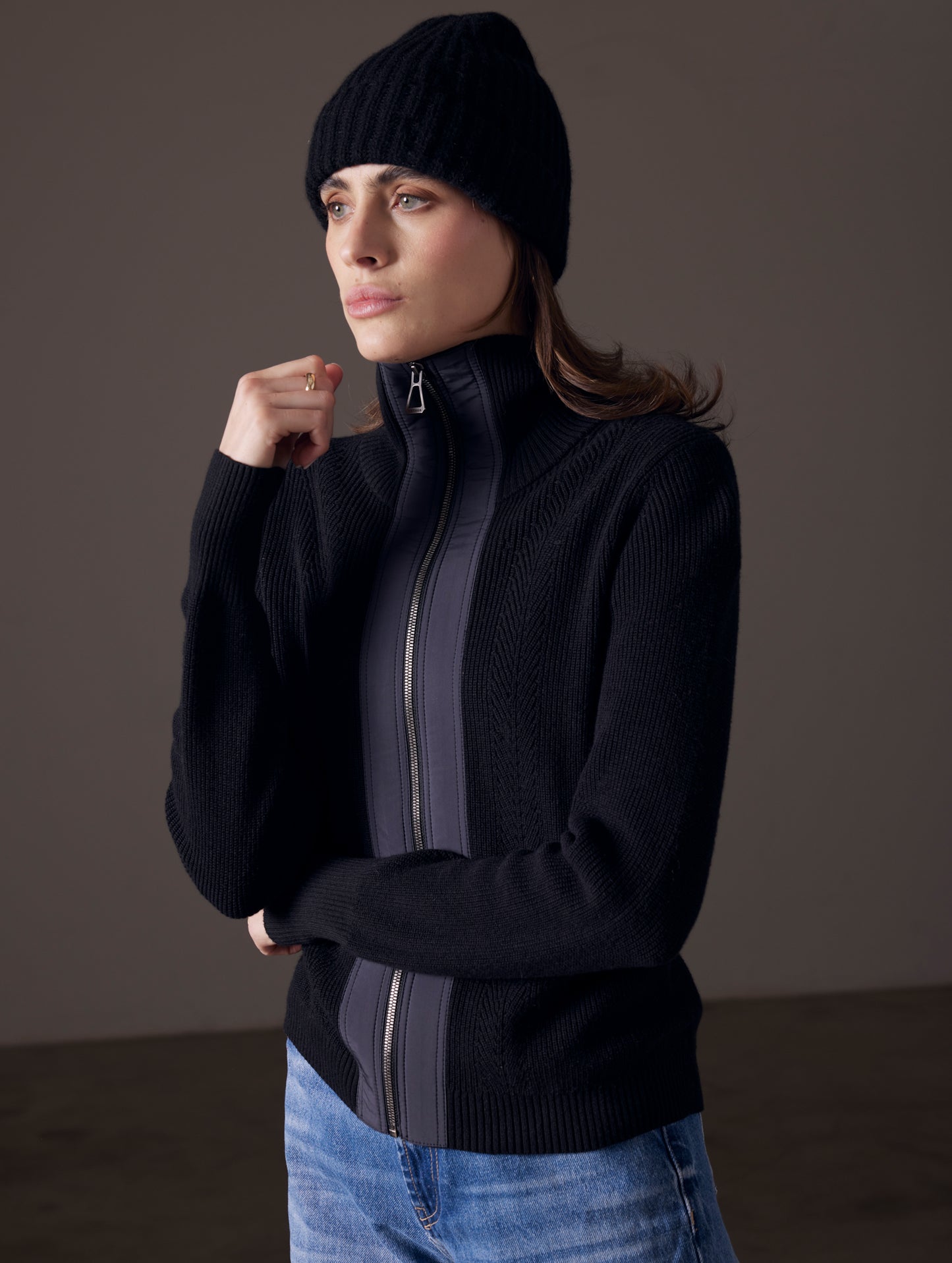 Front angled view of woman wearing black beanie and Rhea Full-Zip Sweater in Onyx Black from AETHER Apparel.