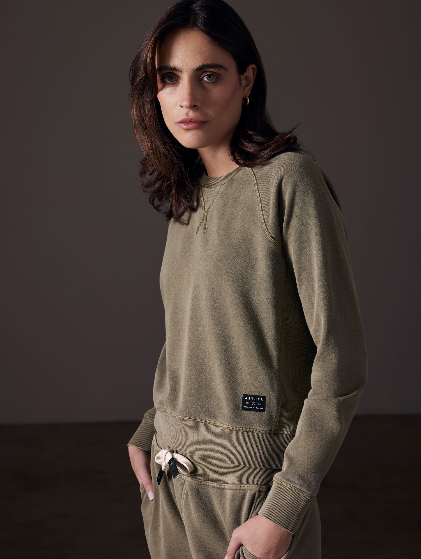 Front angled view of woman wearing Solstice Lightweight Raglan Pullover in Command Green from AETHER Apparel.