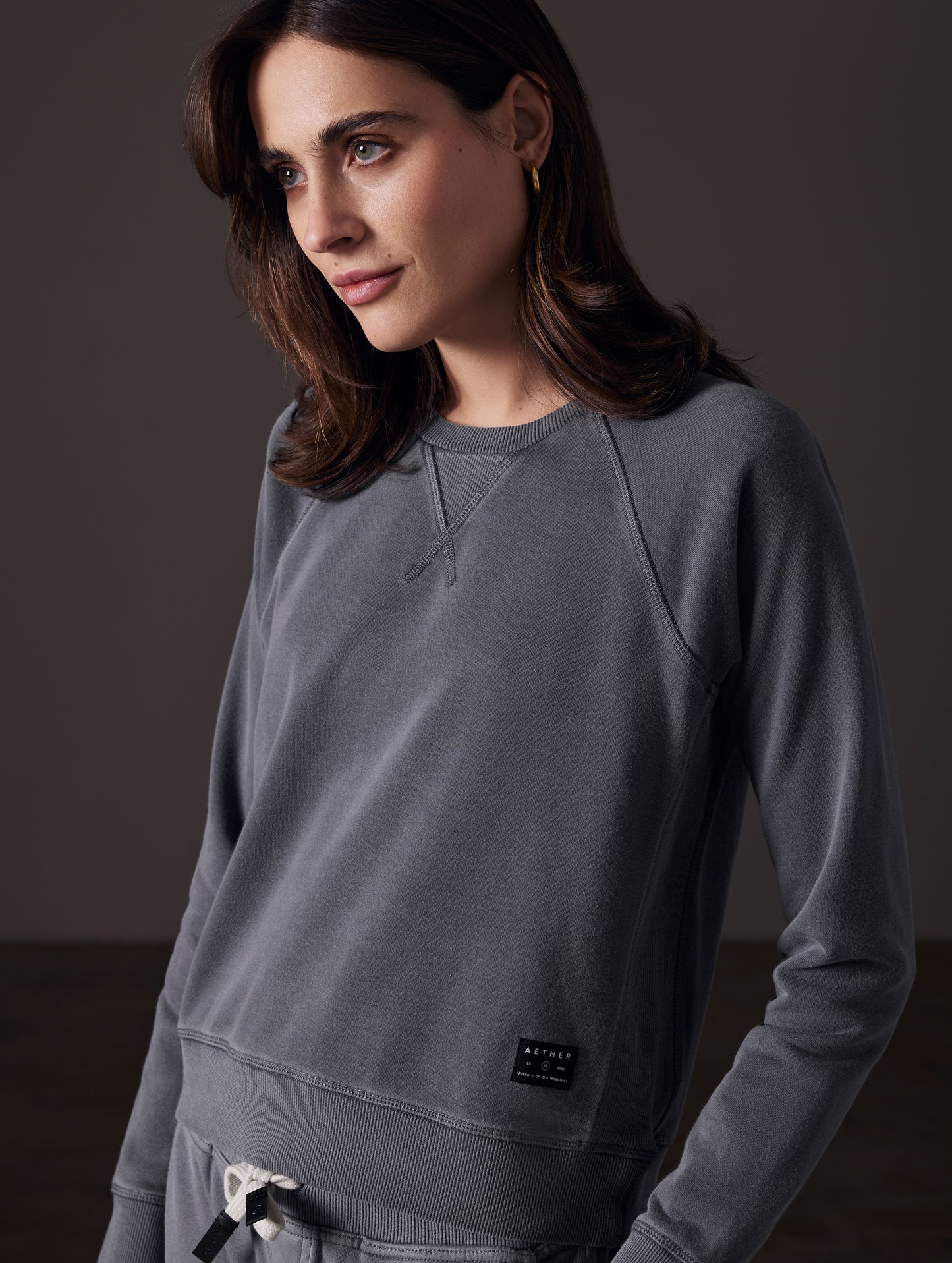 Front angled view of woman wearing Solstice Lightweight Raglan Pullover in Graphite from AETHER Apparel.