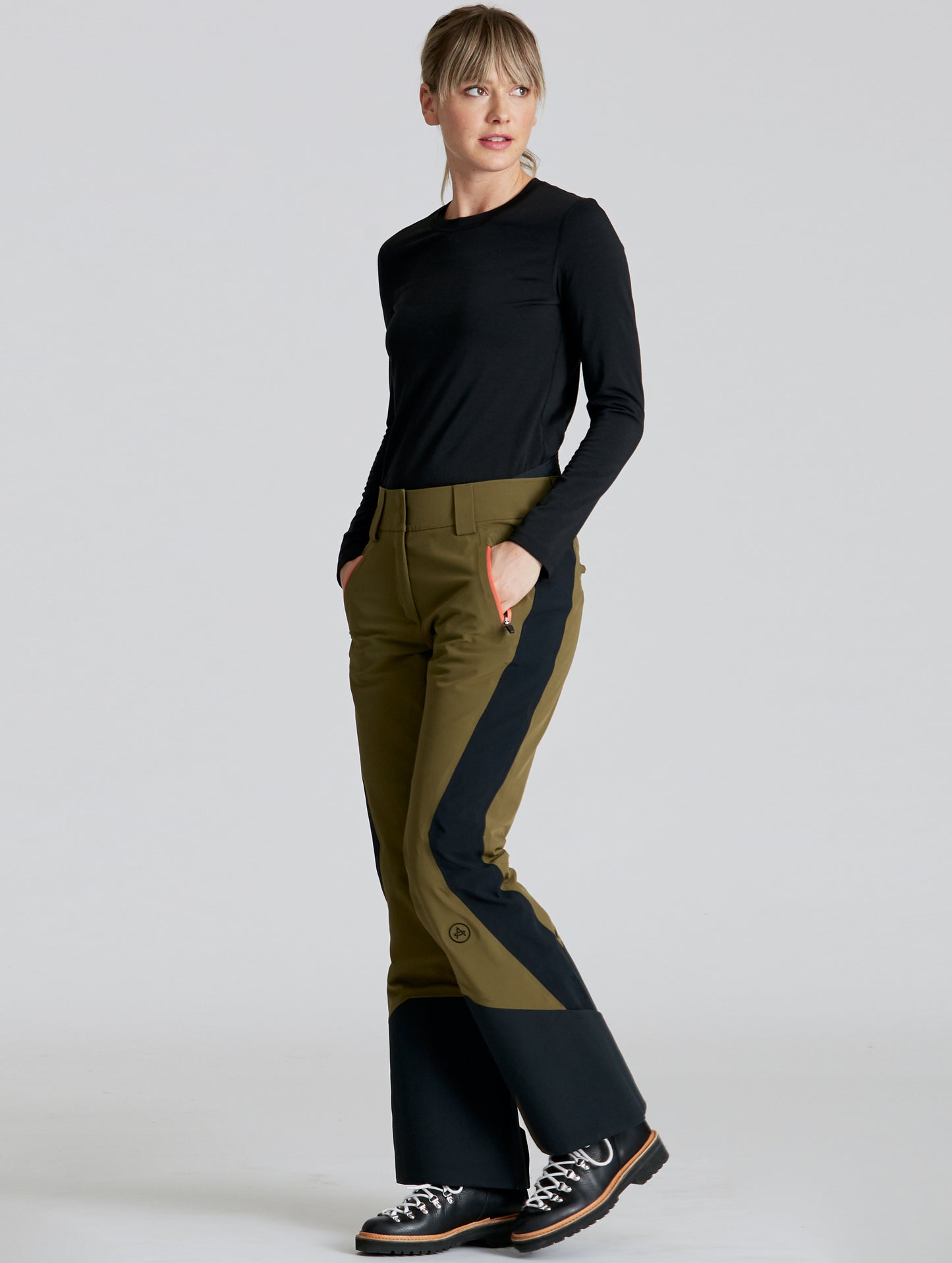 Front angled full-body view of woman wearing Stealth Snow Pant in Command Green and Onyx Black from AETHER Apparel.