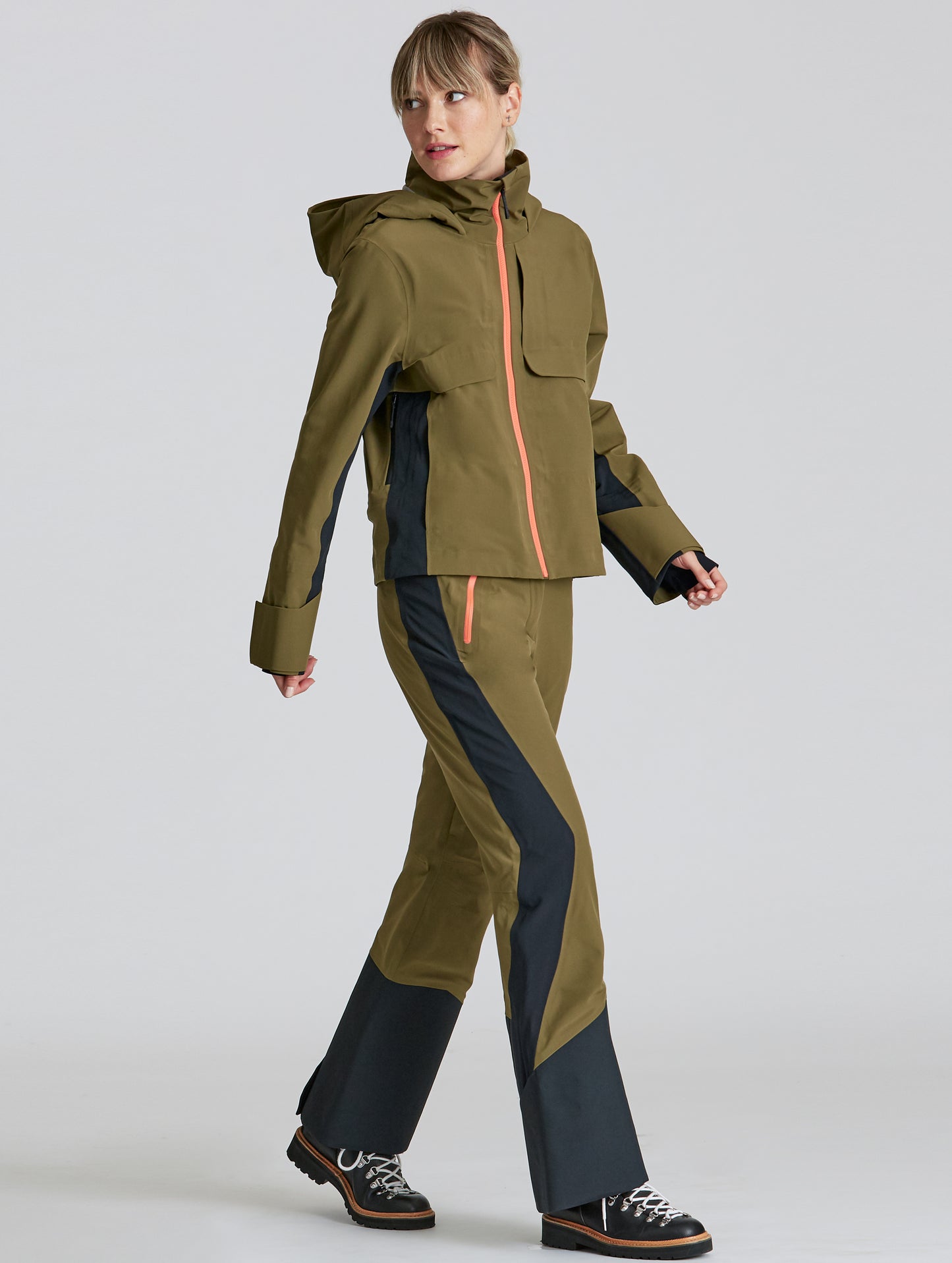 Front angled full-body view of woman walking wearing Stealth Snow Pant and matching jacket in Command Green and Onyx Black from AETHER Apparel.