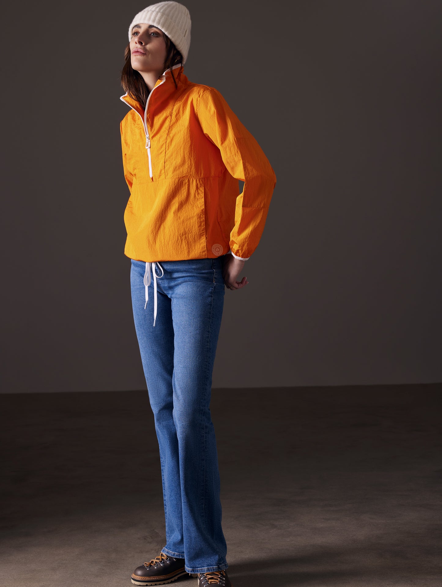 Front angled full-body view of woman wearing Topanga Lightweight Anorak in Midas Orange from AETHER Apparel.