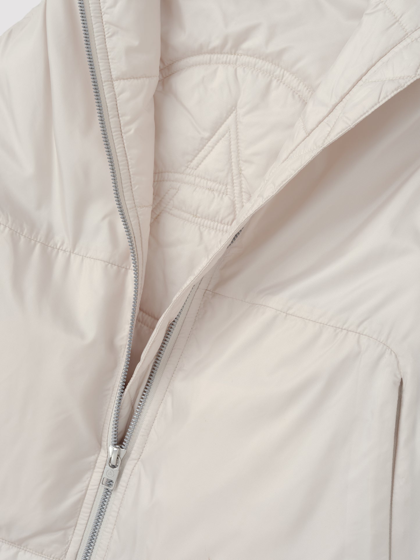 Closeup detailed view of the custom AETHER logo quilting on the interior of the Celeste Eco Insulated Vest in Bone from AETHER Apparel.