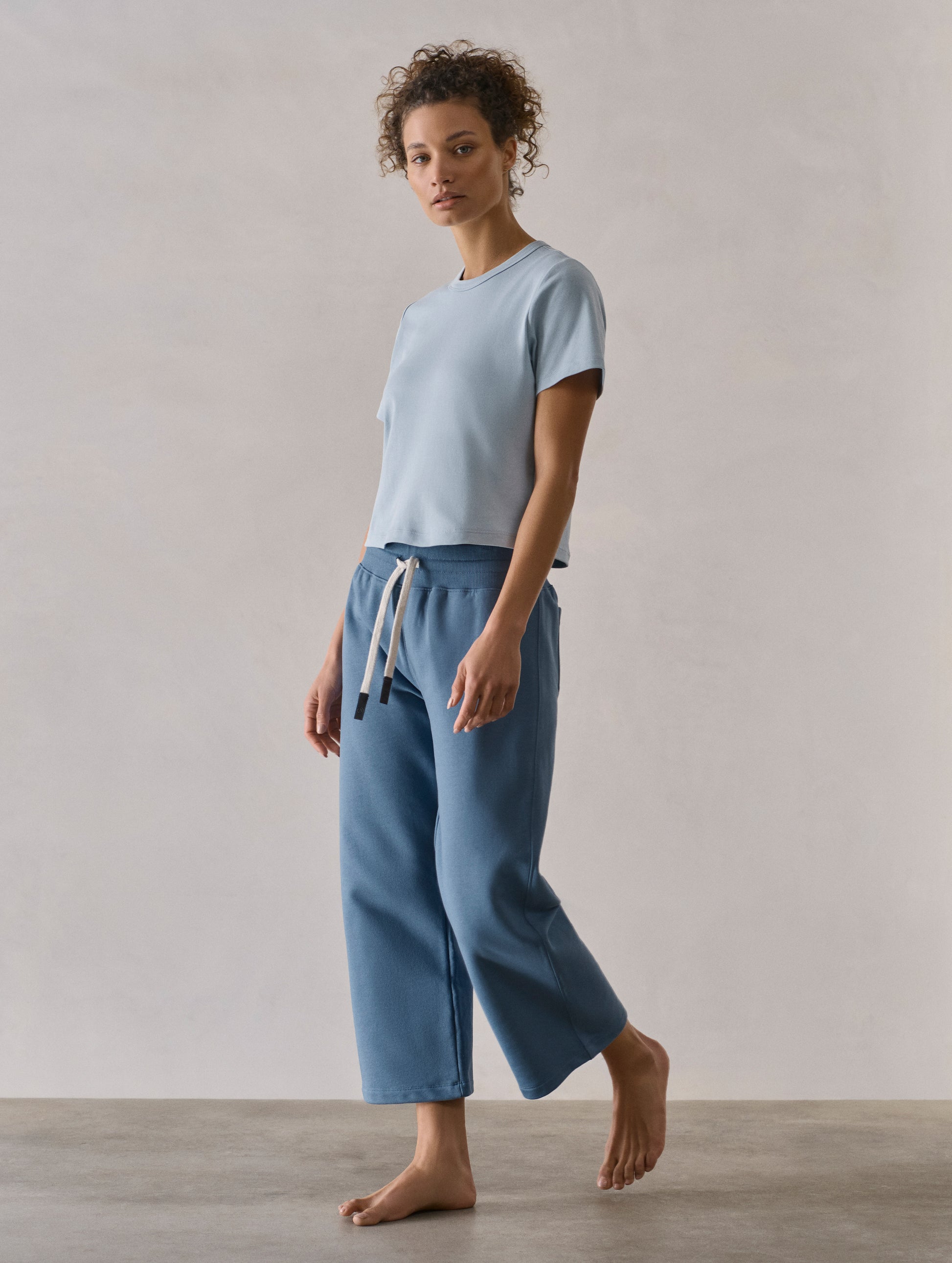 Front 3/4 full-body view of woman wearing W Osa Cropped Sweatpant in Coastal Blue from AETHER Apparel.