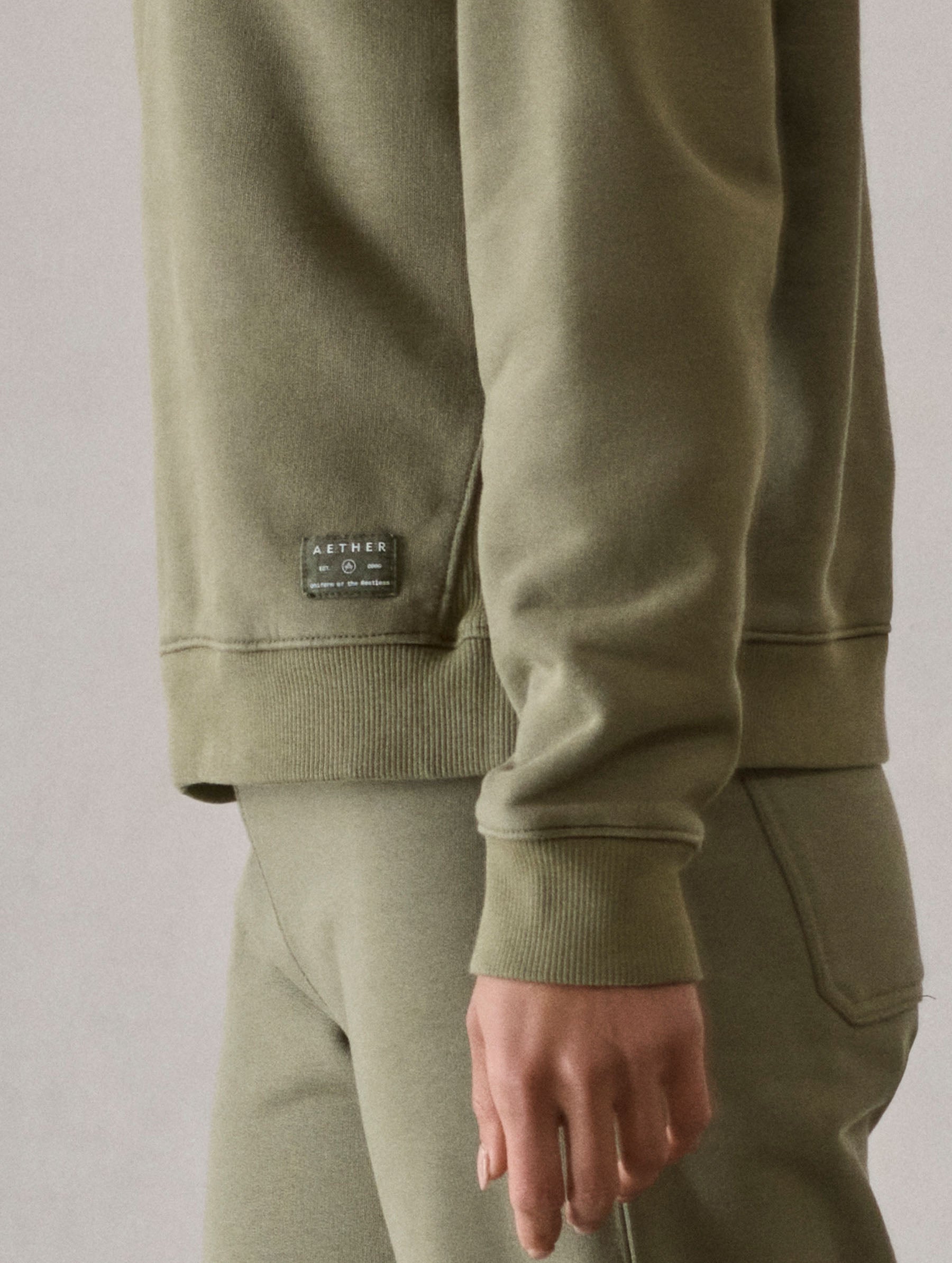 Closeup detailed view of the elasticated cuff and AETHER label tag on the W Osa Raglan Sweatshirt in Fern Green from AETHER Apparel.