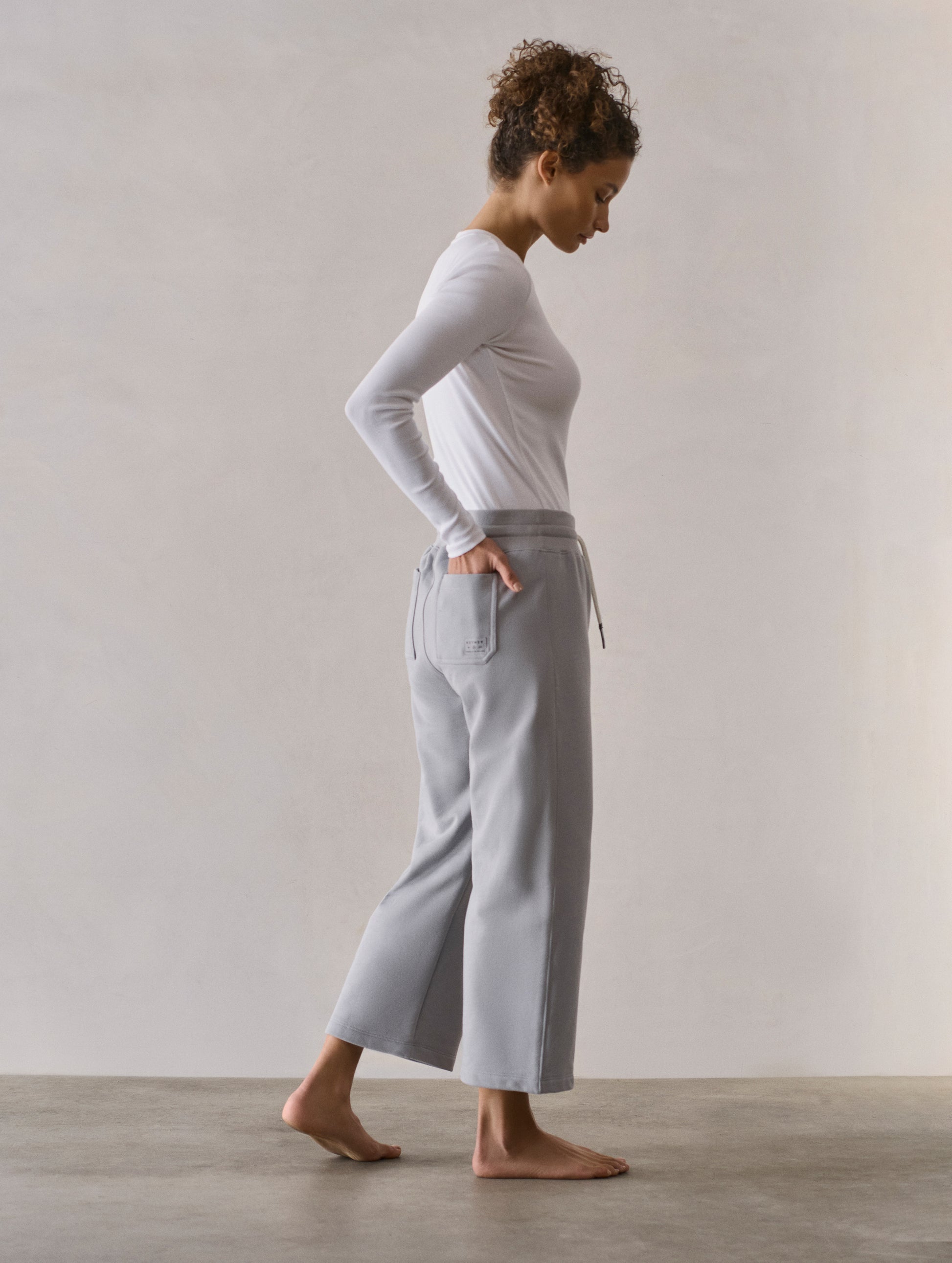 Right side profile full-body view of woman wearing W Osa Cropped Sweatpant in Sky Grey from AETHER Apparel.