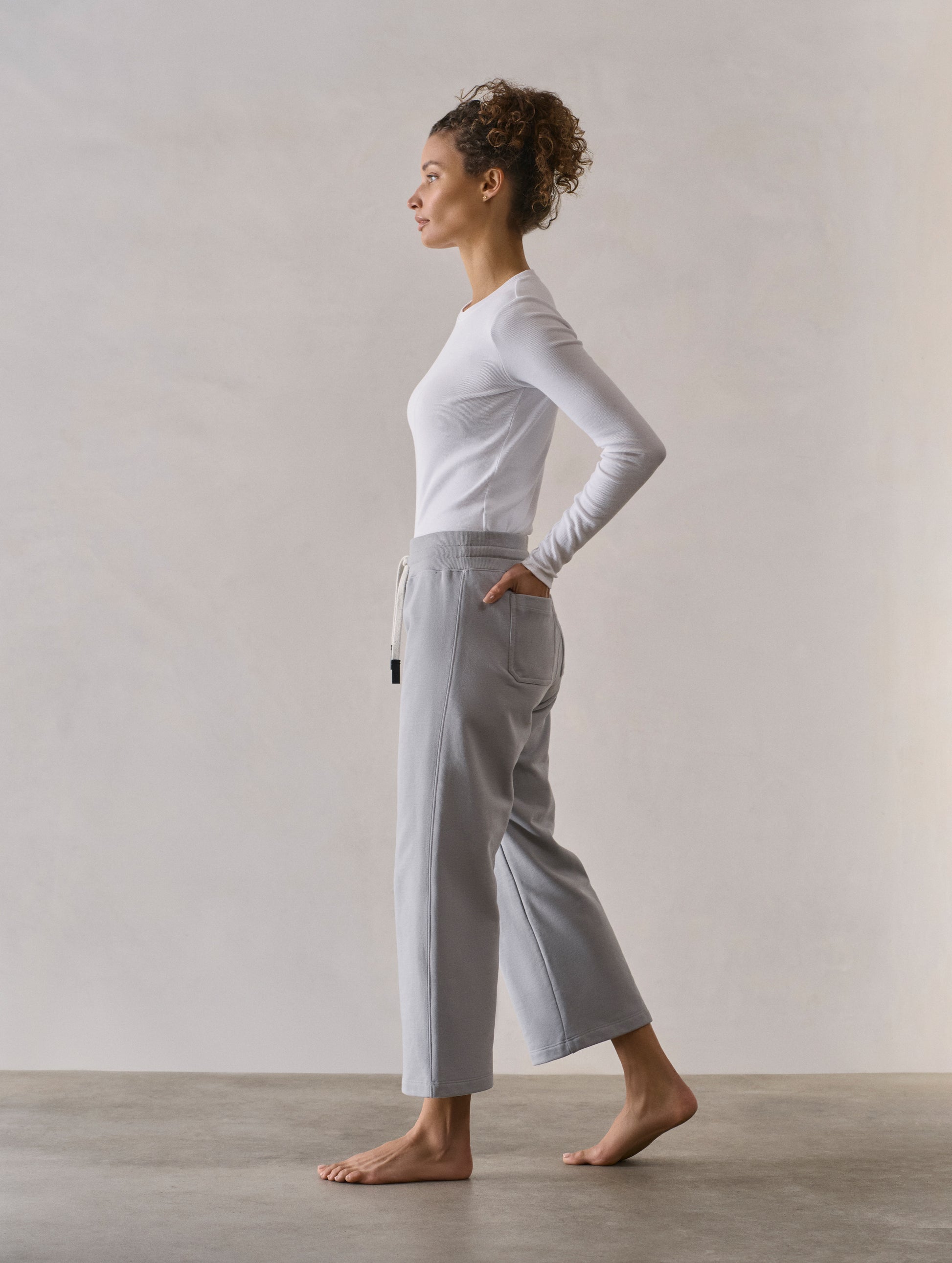 Left side profile full-body view of woman wearing W Osa Cropped Sweatpant in Sky Grey from AETHER Apparel.