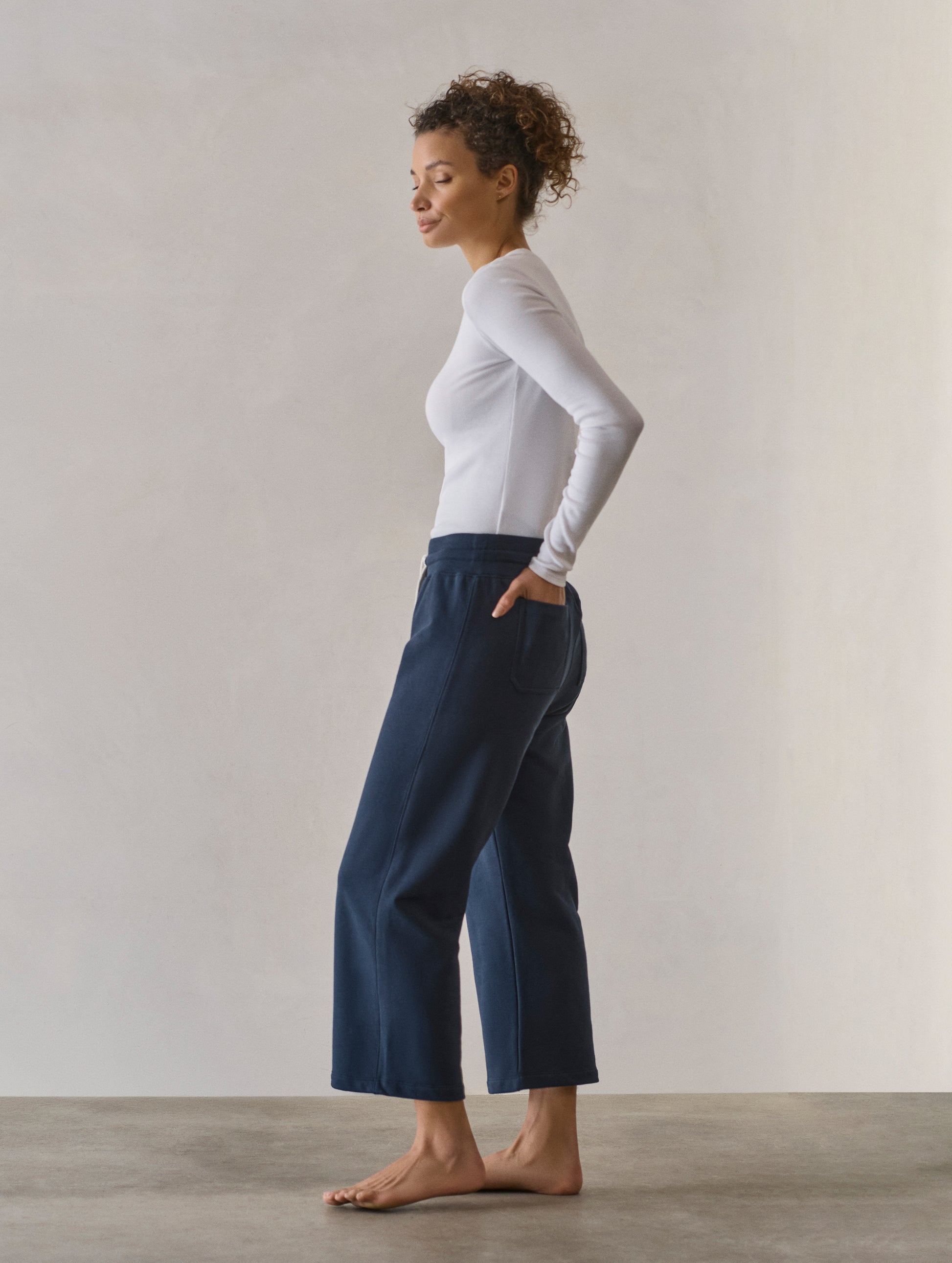 Left side profile full-body view of woman wearing W Osa Cropped Sweatpant in Total Eclipse dark blue from AETHER Apparel.