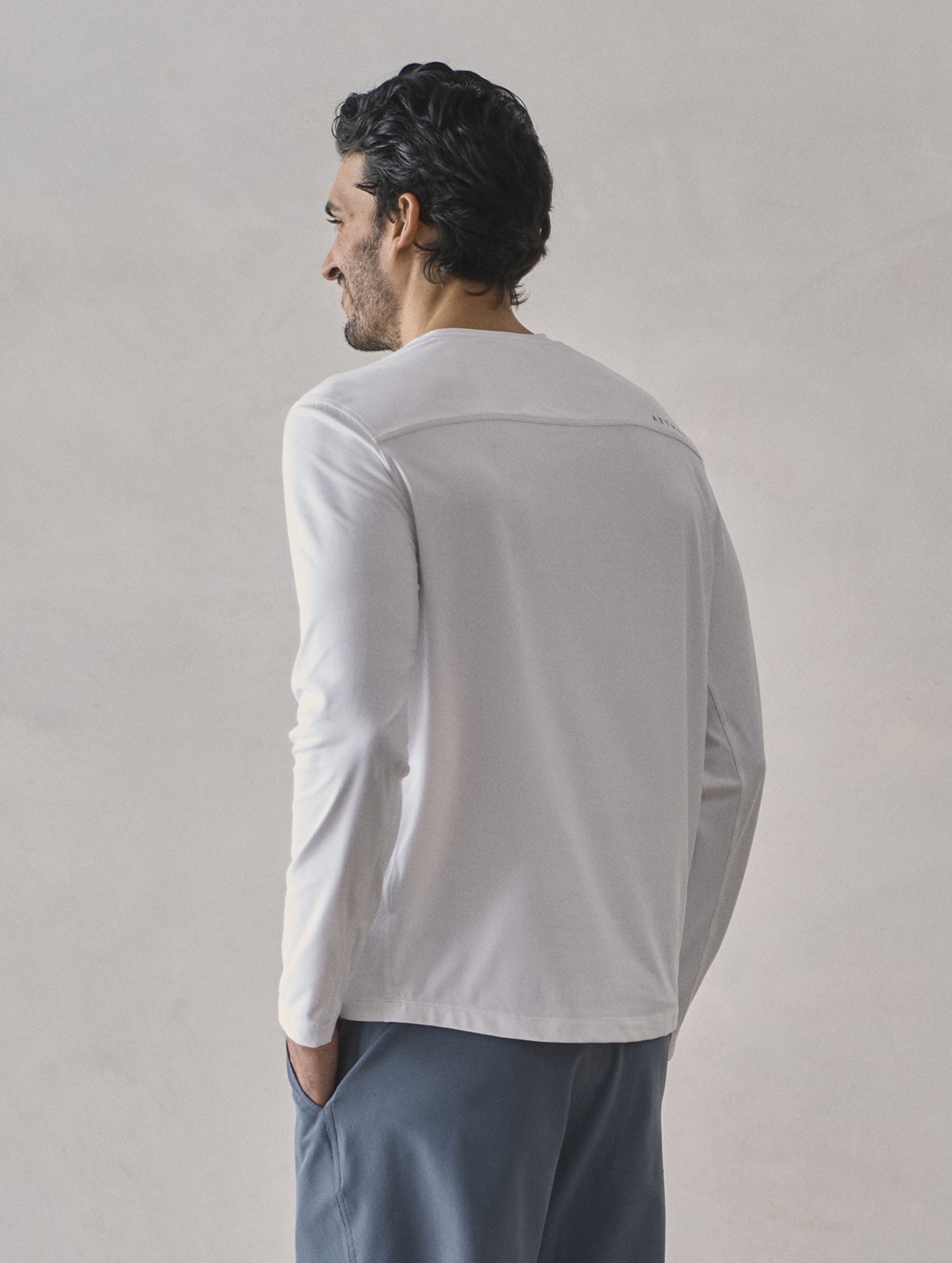 Rear 3/4 upper-body view of man wearing Adventure Performance Long-Sleeve Tee in White from AETHER Apparel.