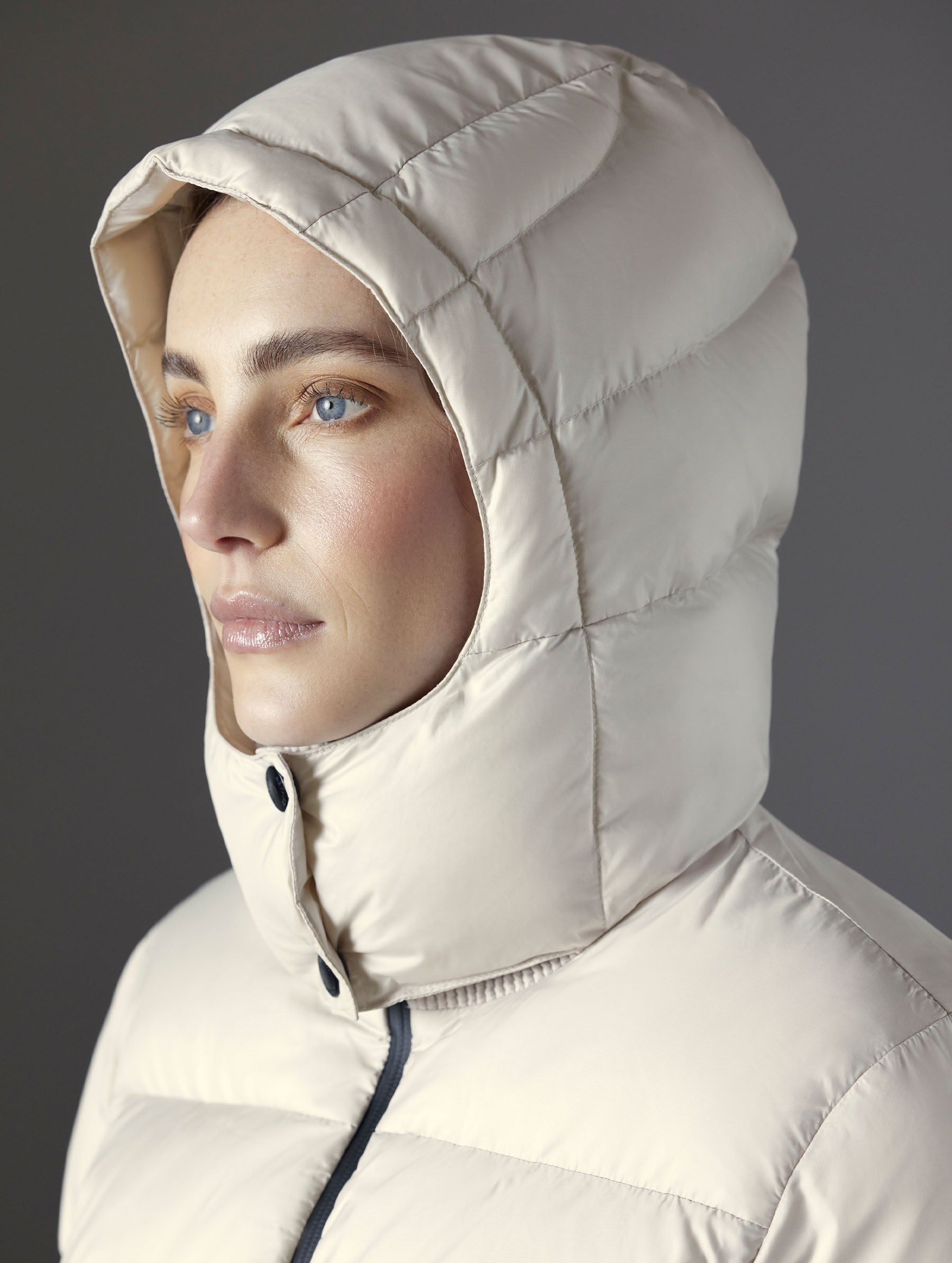 Closeup detailed view of woman wearing the snap-secured, quilted, 4-piece hood on the Aura Puffer Jacket in Bone white from AETHER Apparel.