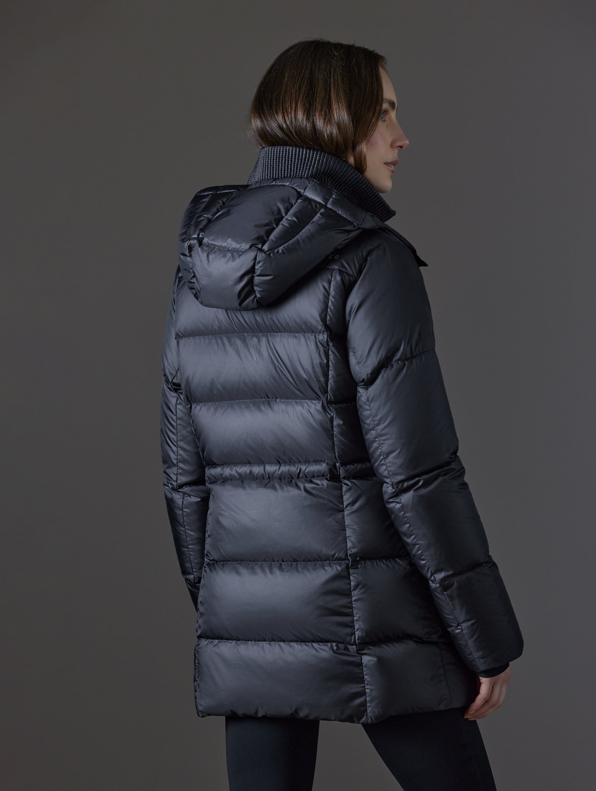 Rear angled view of woman wearing Aura Puffer Long in Onyx Black from AETHER Apparel.