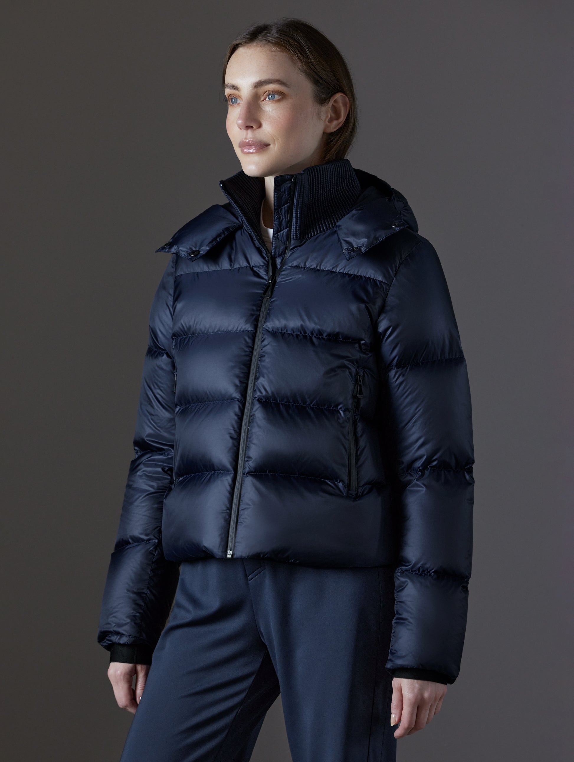 Front angled view of woman wearing Aura Puffer Jacket in Total Eclipse dark blue from AETHER Apparel.