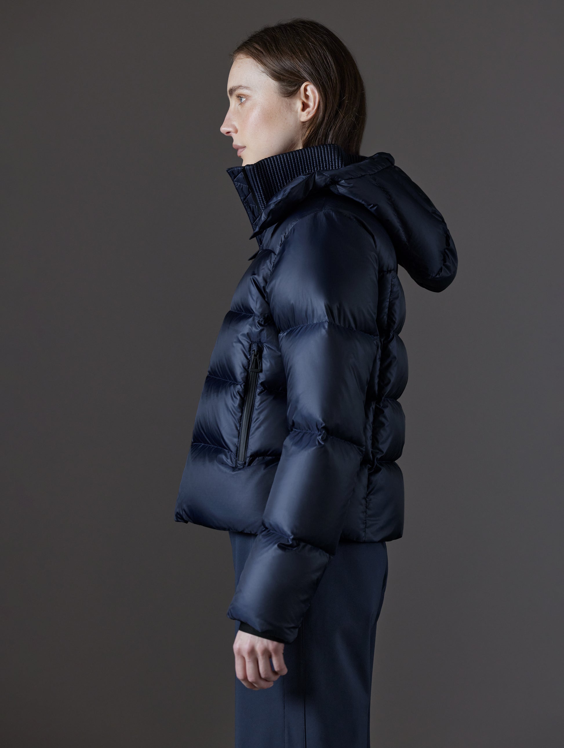 Side profile view of woman wearing Aura Puffer Jacket in Total Eclipse dark blue from AETHER Apparel.