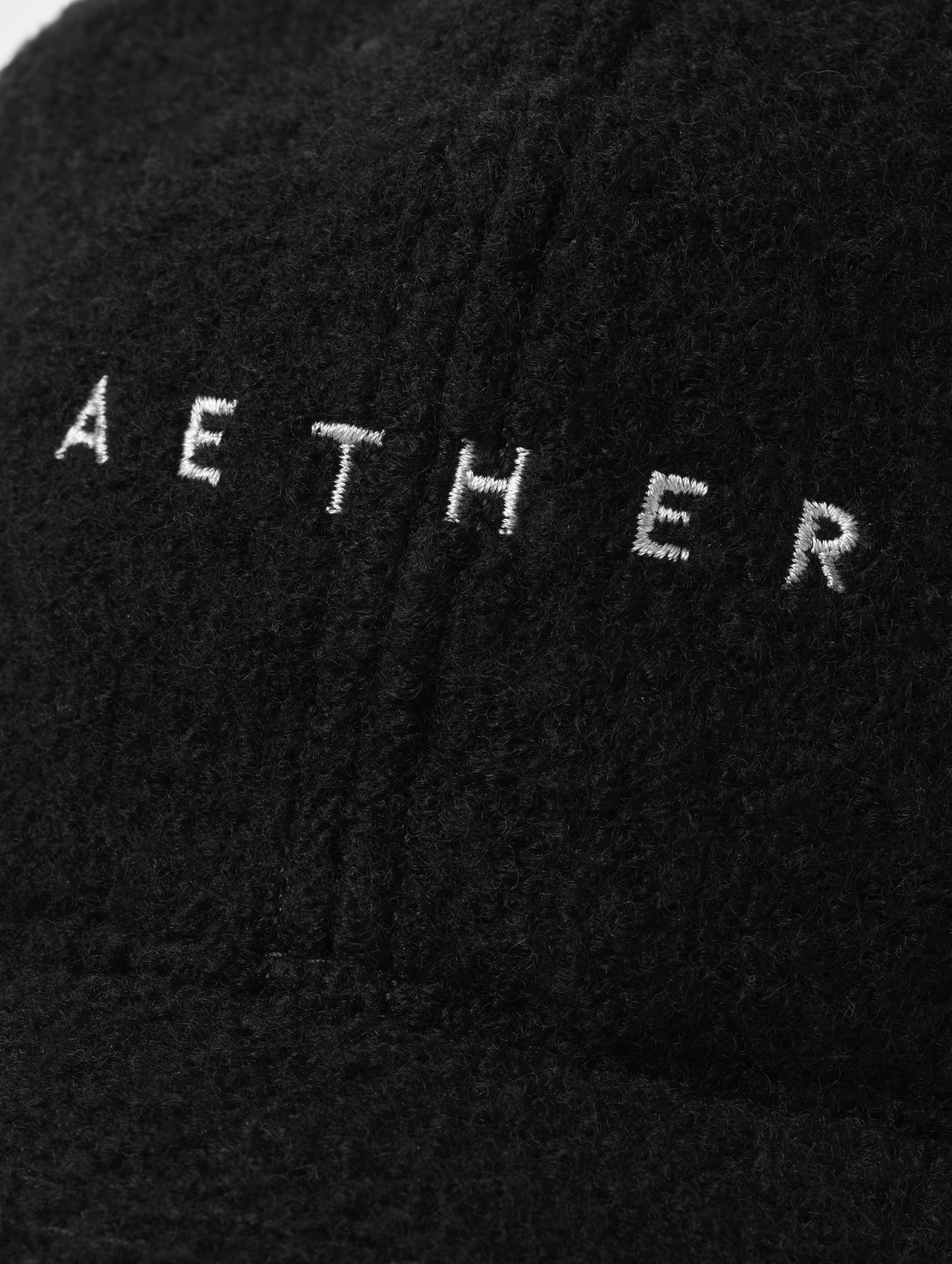 Closeup detailed view of the embroidered wordmark on the front of the Aura Wool Hat in Onyx Black from AETHER Apparel. 