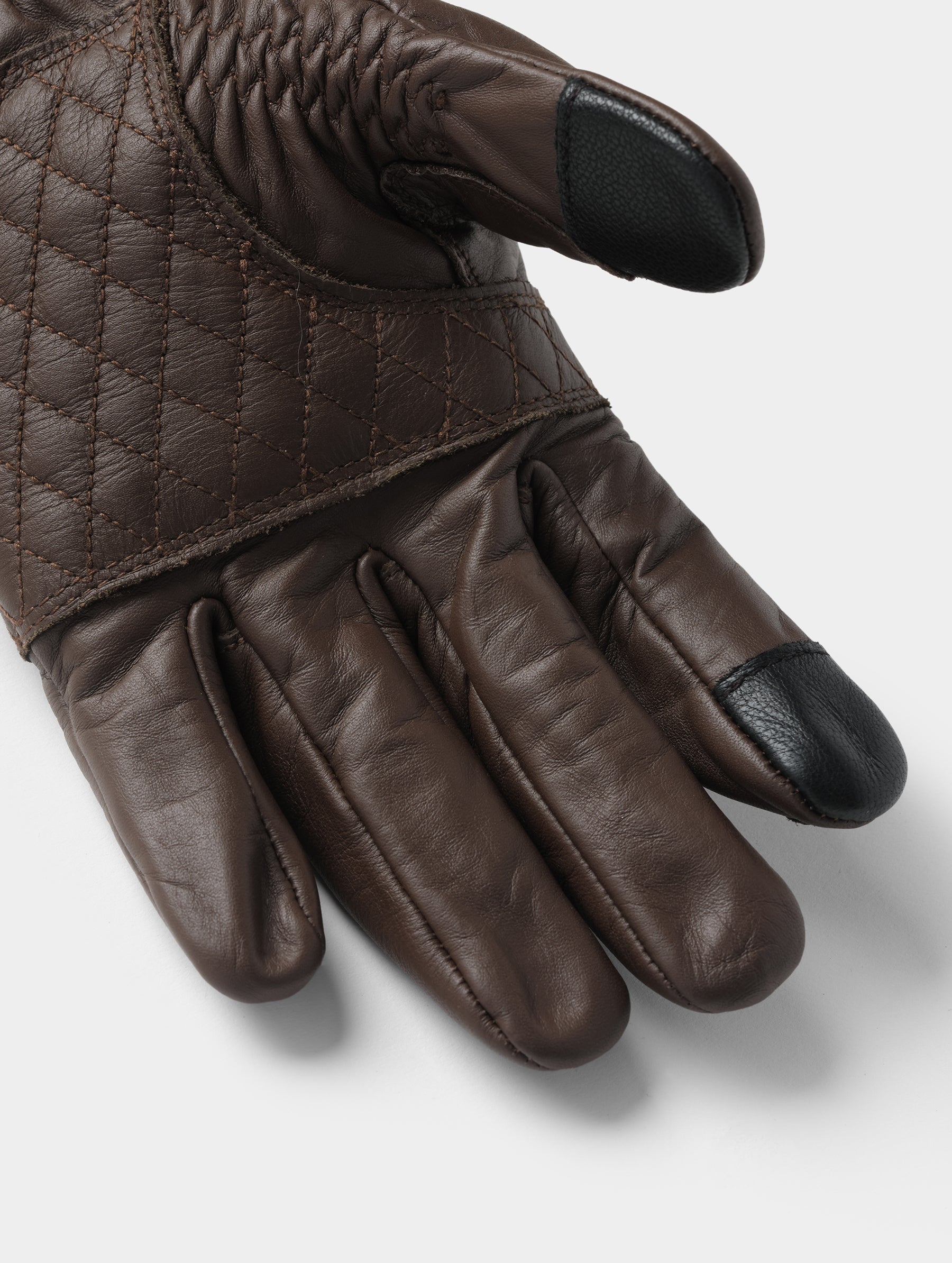Closeup detailed view of the diamond-quilted palm and conductive thumb and pointer fingertips on the Circuit Moto Glove in Espresso Brown from AETHER Apparel.