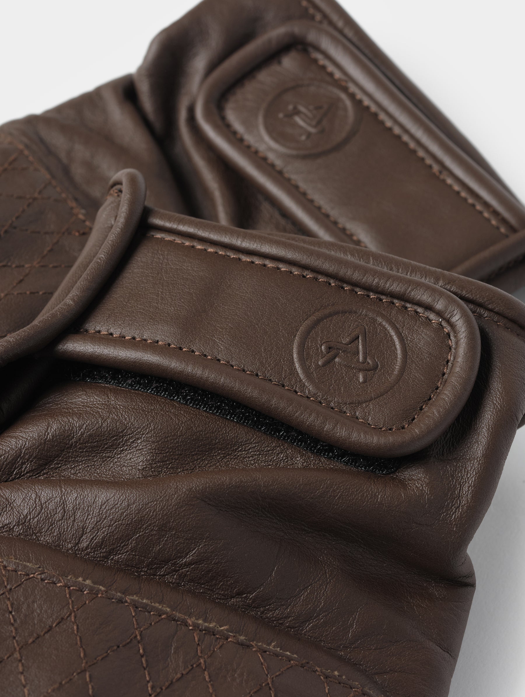 Closeup detailed view of the elasticated wrist and embossed AETHER-branded Velcro pull tab on the Circuit Moto Glove in Espresso Brown from AETHER Apparel.