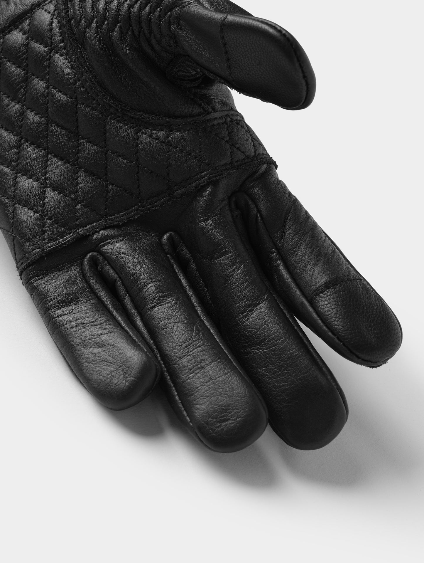 Closeup detailed view of the diamond-quilted palm and conductive thumb and pointer fingertips on the Circuit Moto Glove in Onyx Black from AETHER Apparel.