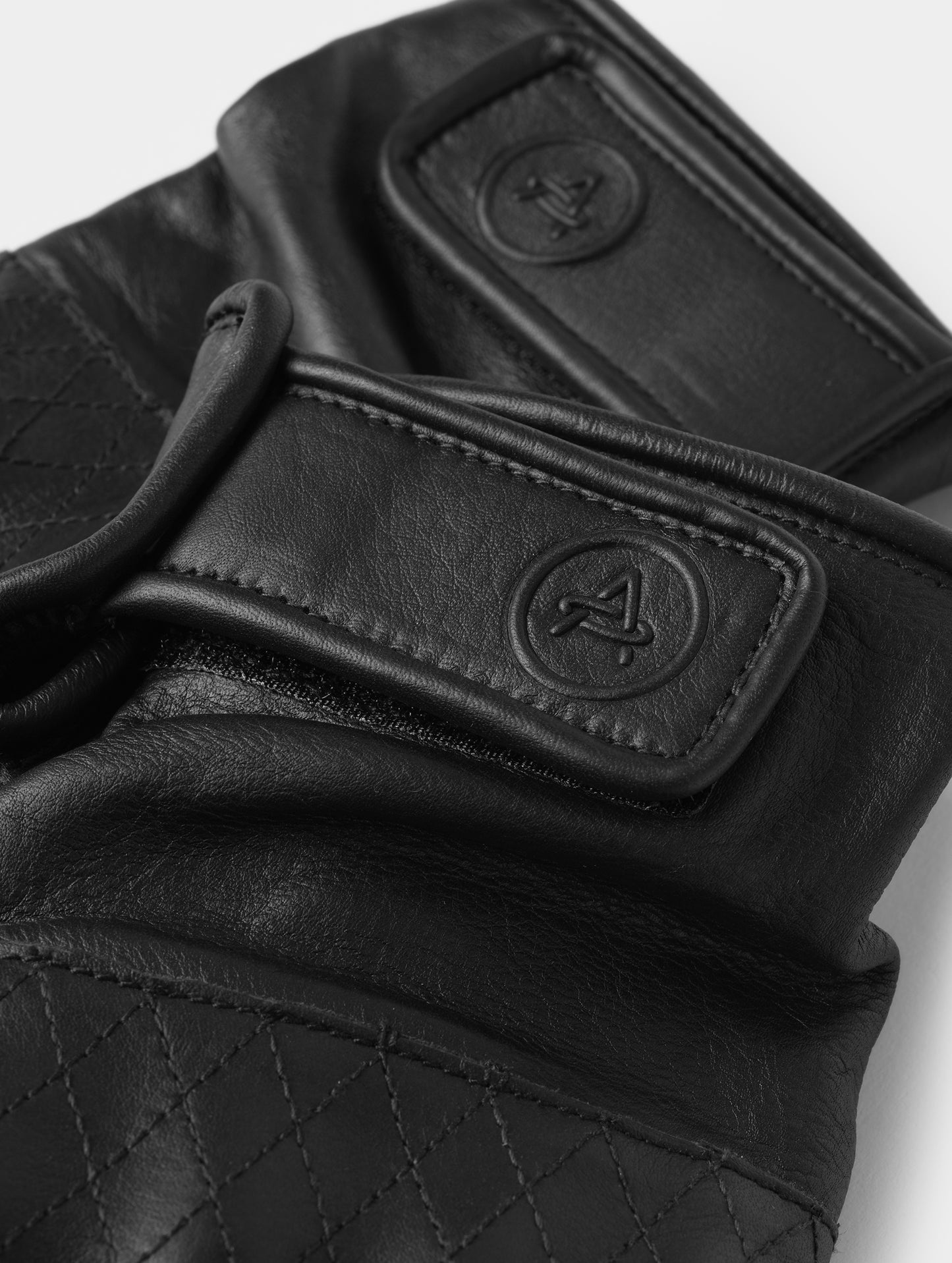 Closeup detailed view of the elasticated wrist and embossed AETHER-branded Velcro pull tab on the Circuit Moto Glove in Onyx Black from AETHER Apparel. 