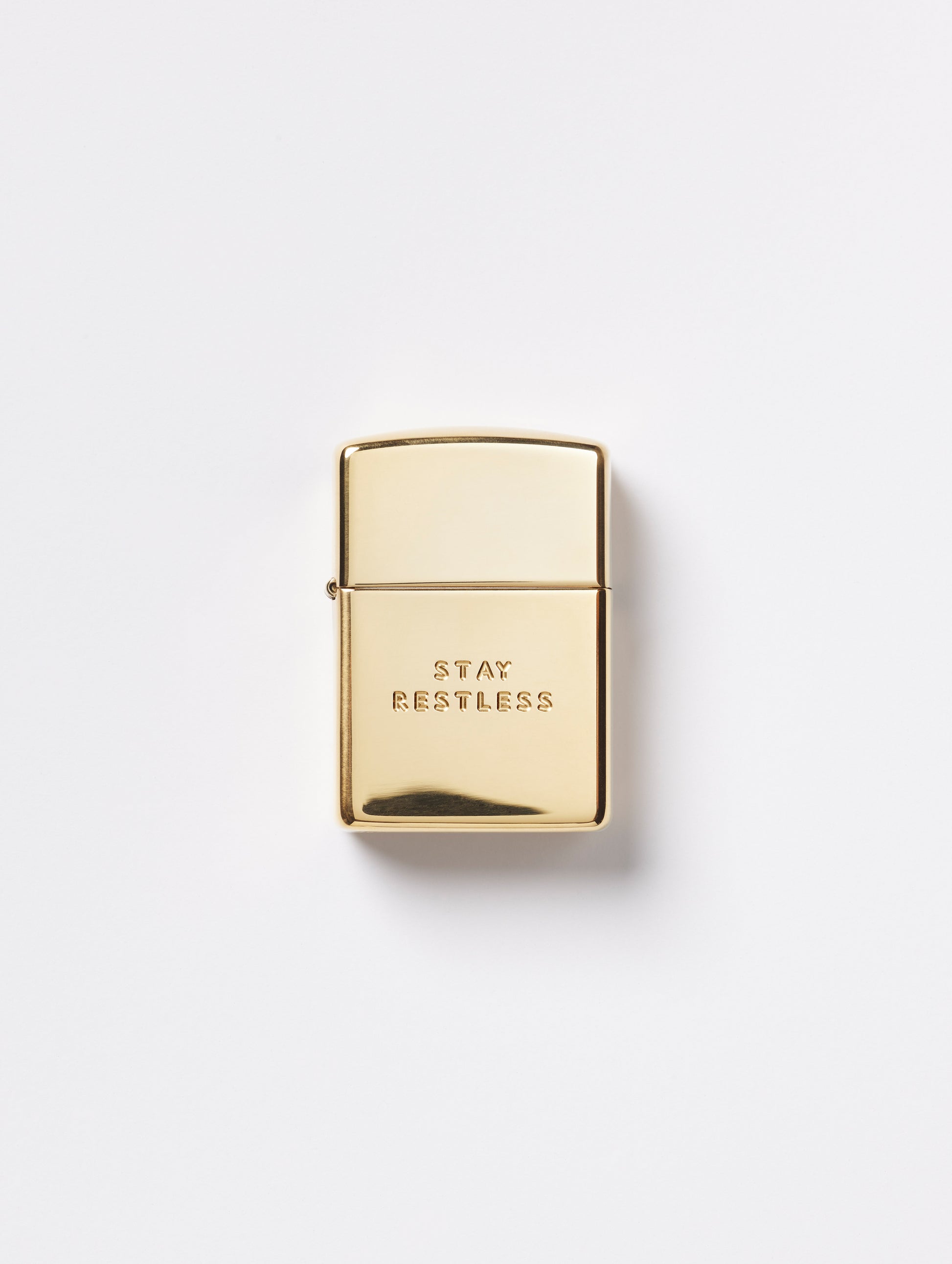 Flay lay view of front of Restless Zippo Lighter in high polish brass from AETHER Apparel with top closed. 