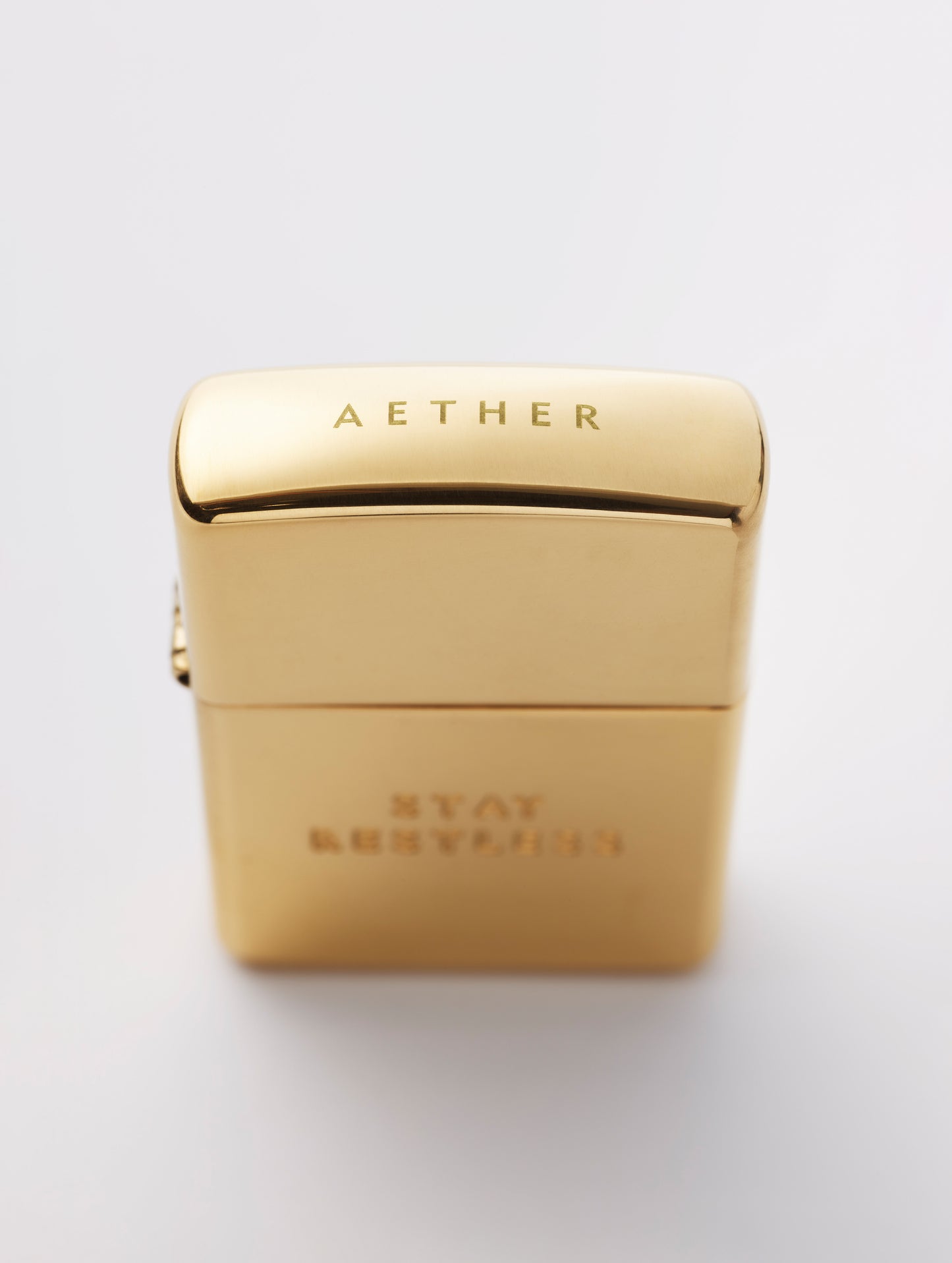 Top angled view of AETHER logo on cap of Restless Zippo Lighter in high polish brass from AETHER Apparel with top closed. 