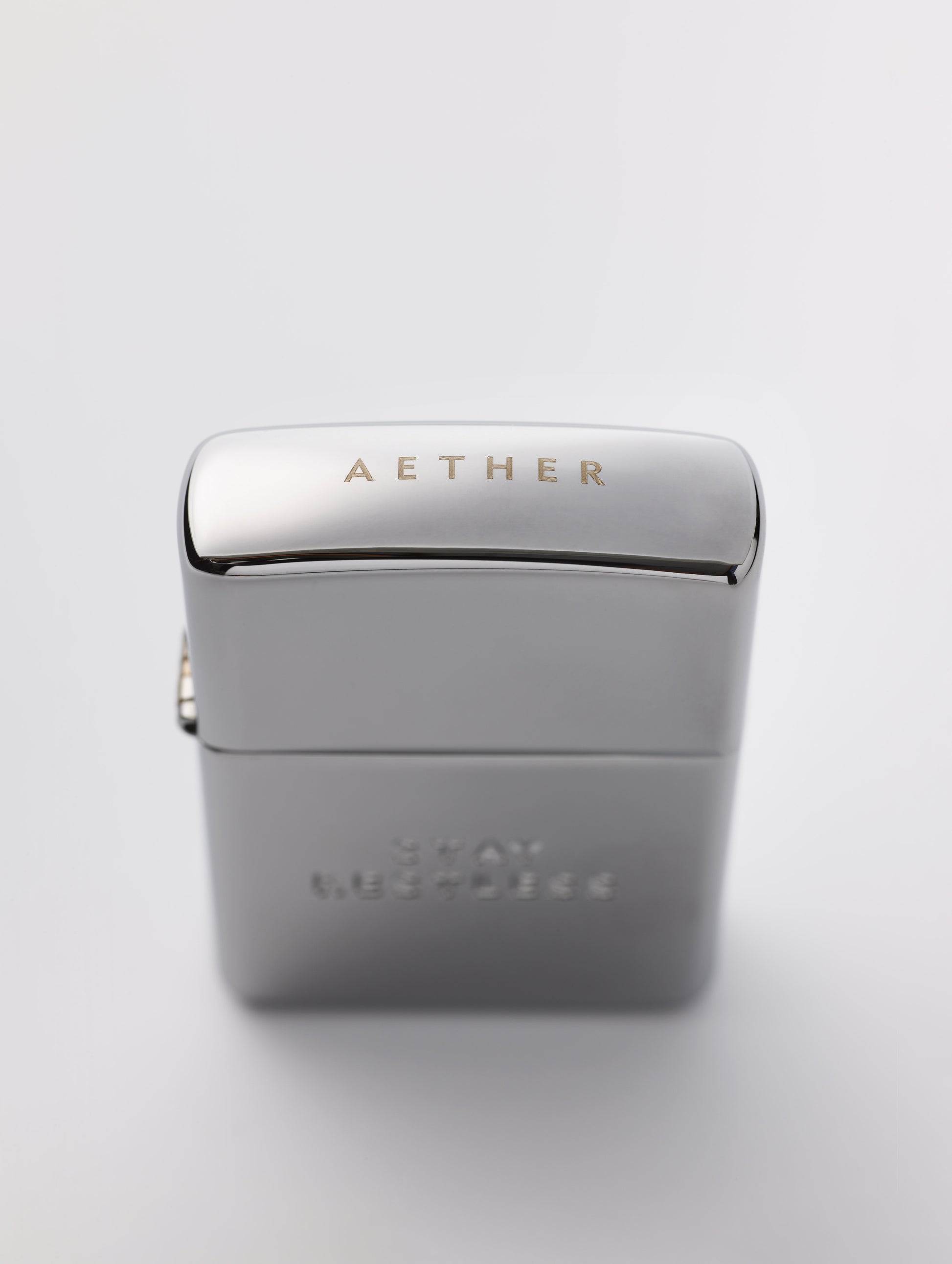 Top angled view of AETHER logo on cap of Restless Zippo Lighter in high polish chrome from AETHER Apparel with top closed. 