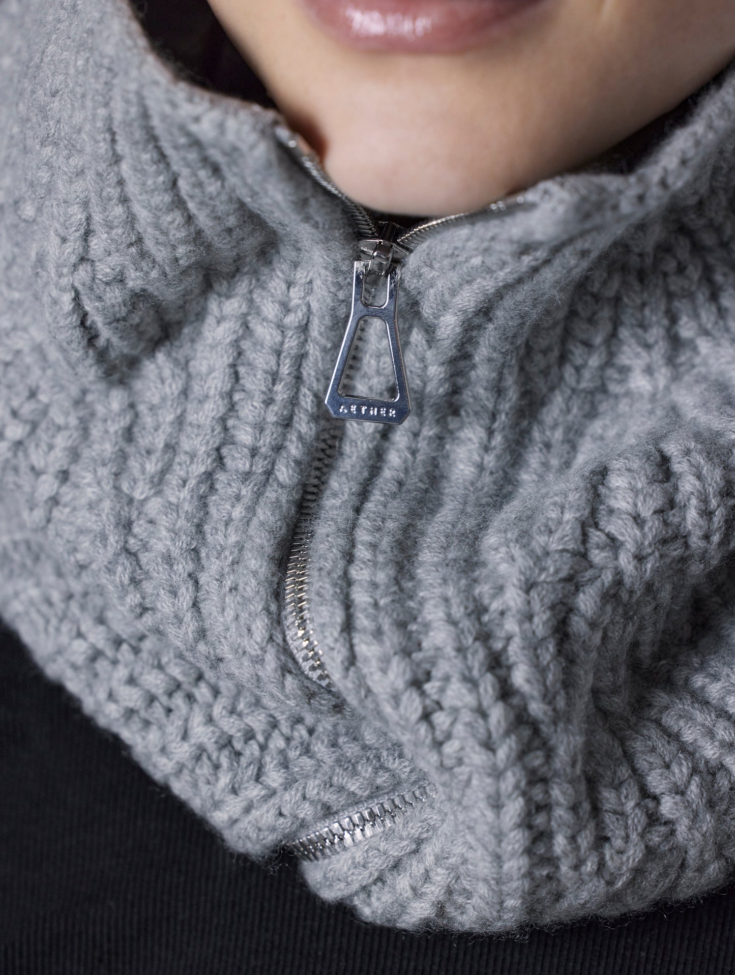 Closeup detailed view of zipper, custom zipper pull, and knitted construction of Sweater Neck Gaiter 2.0 in Light Heather Grey from AETHER Apparel. 