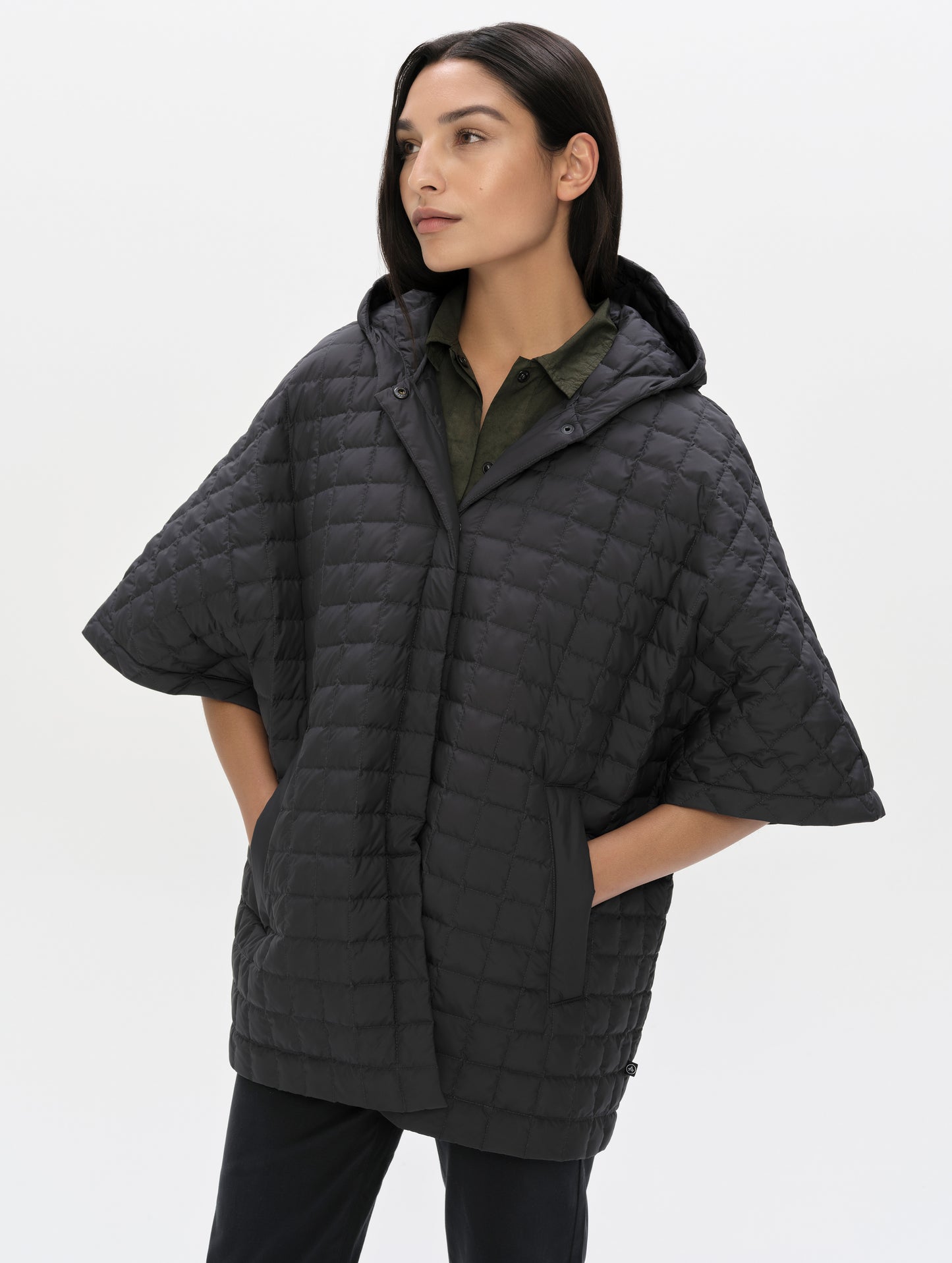 Front, angled upper-body view of woman with hood down wearing the Bardo Hooded Poncho in Onyx Black from AETHER Apparel.
