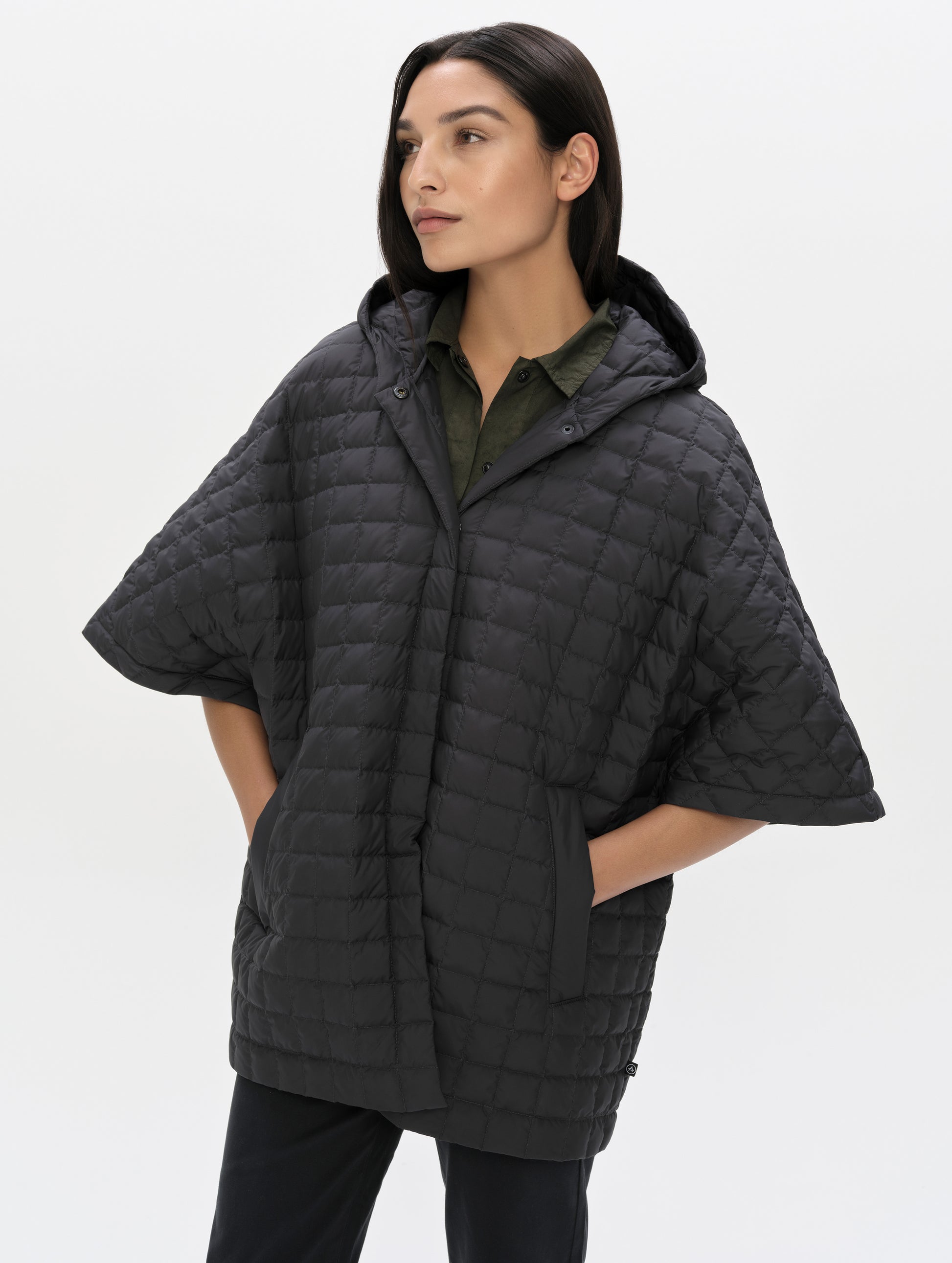 Front, angled upper-body view of woman with hood down wearing the Bardo Hooded Poncho in Onyx Black from AETHER Apparel.