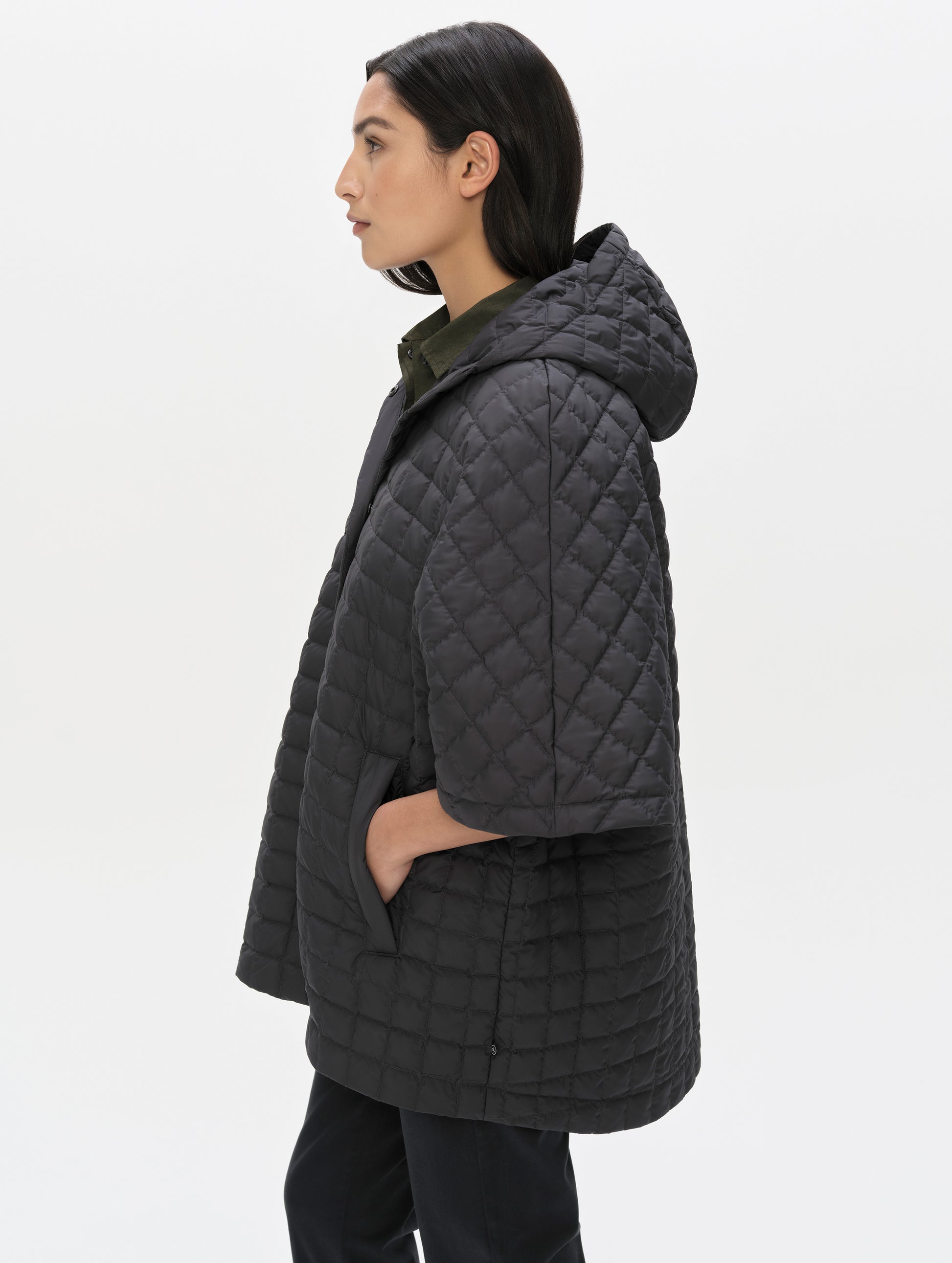 Side profile upper-body view of woman with hood down wearing the Bardo Hooded Poncho in Onyx Black from AETHER Apparel.