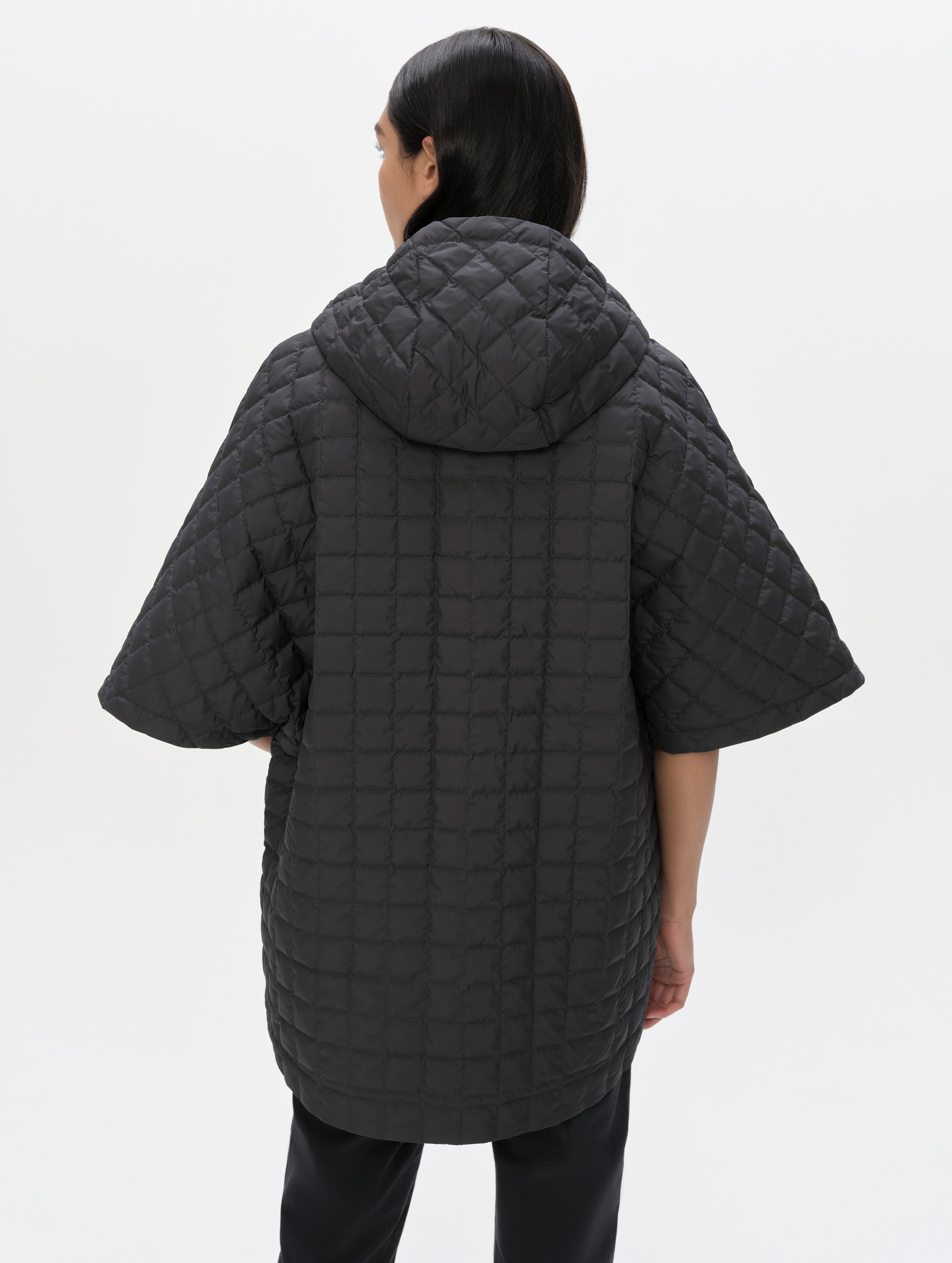 Rear upper-body view of woman with hood down wearing the Bardo Hooded Poncho in Onyx Black from AETHER Apparel.