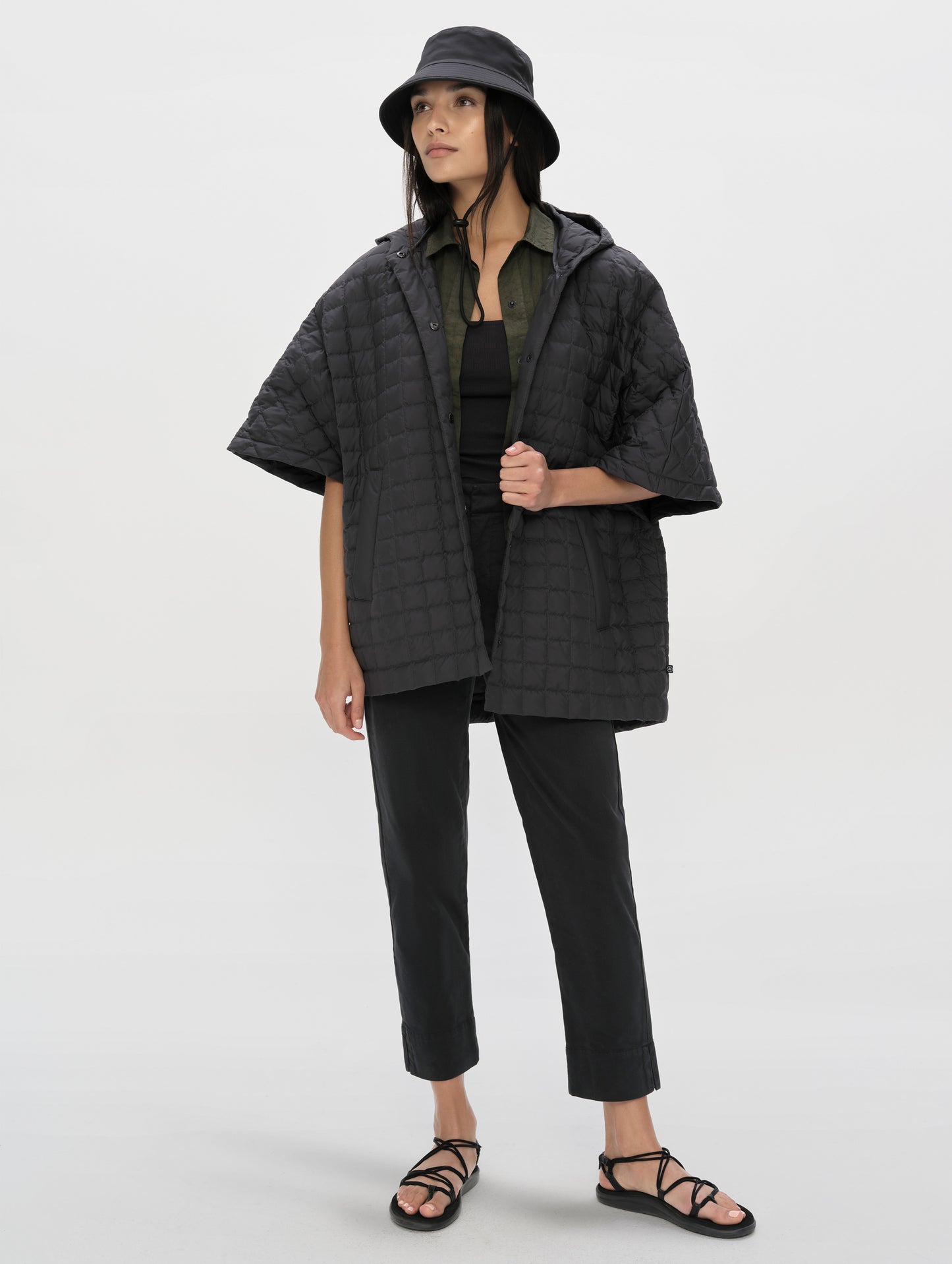 Front, full-body view of woman with hood down wearing the Bardo Hooded Poncho in Onyx Black from AETHER Apparel.