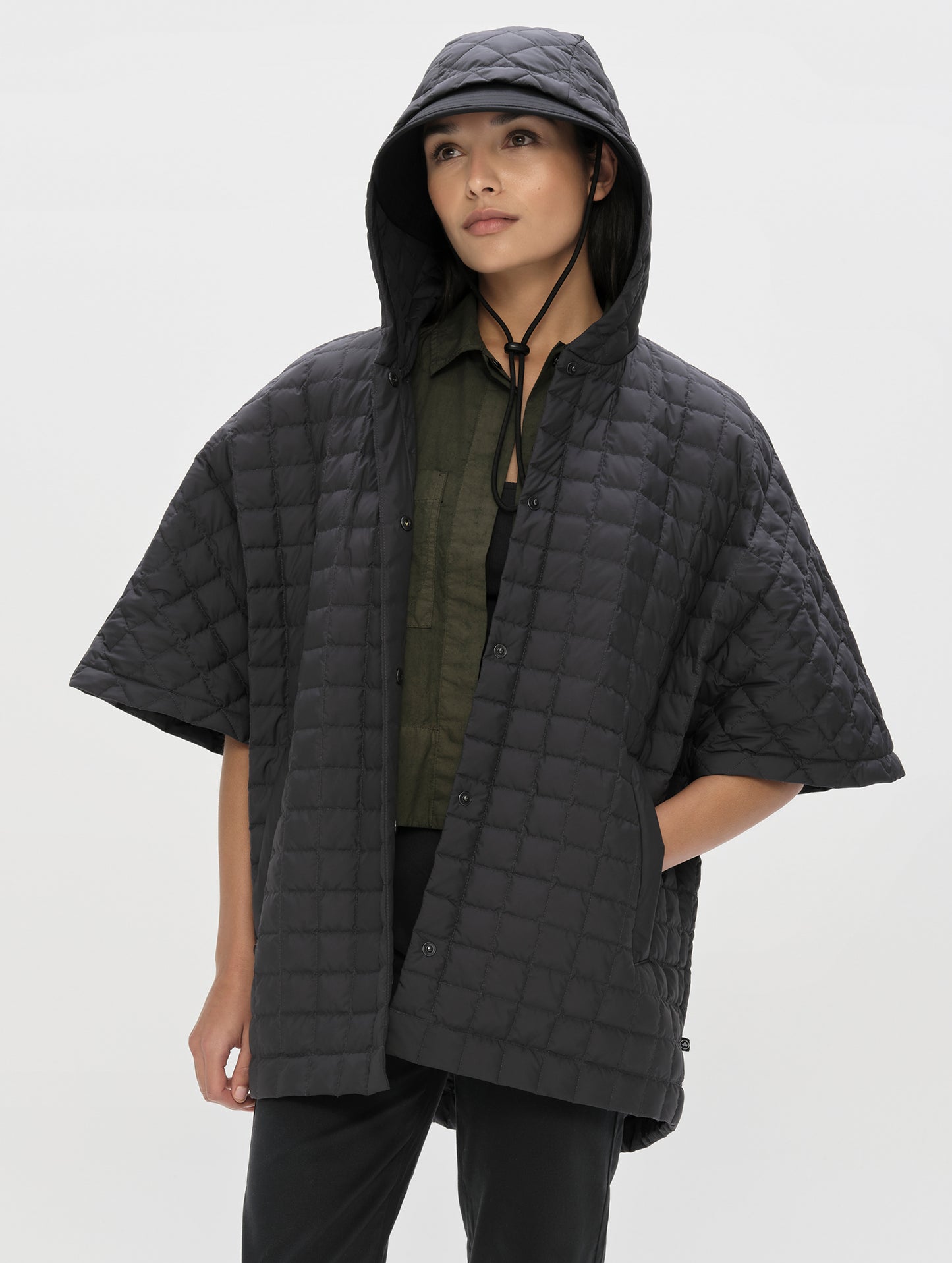 Front, angled upper-body view of woman with hood up wearing the Bardo Hooded Poncho in Onyx Black from AETHER Apparel.