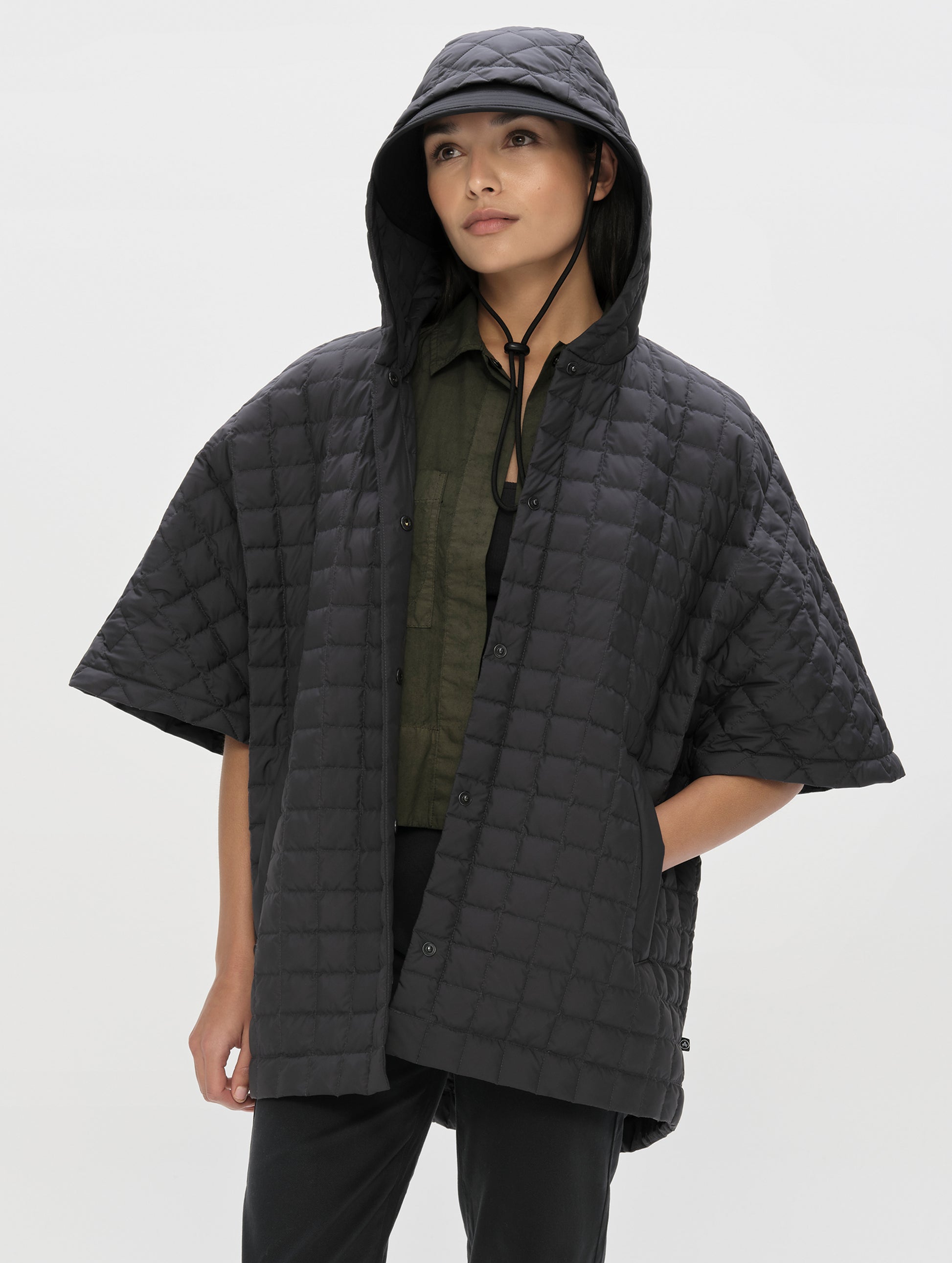 Front, angled upper-body view of woman with hood up wearing the Bardo Hooded Poncho in Onyx Black from AETHER Apparel.
